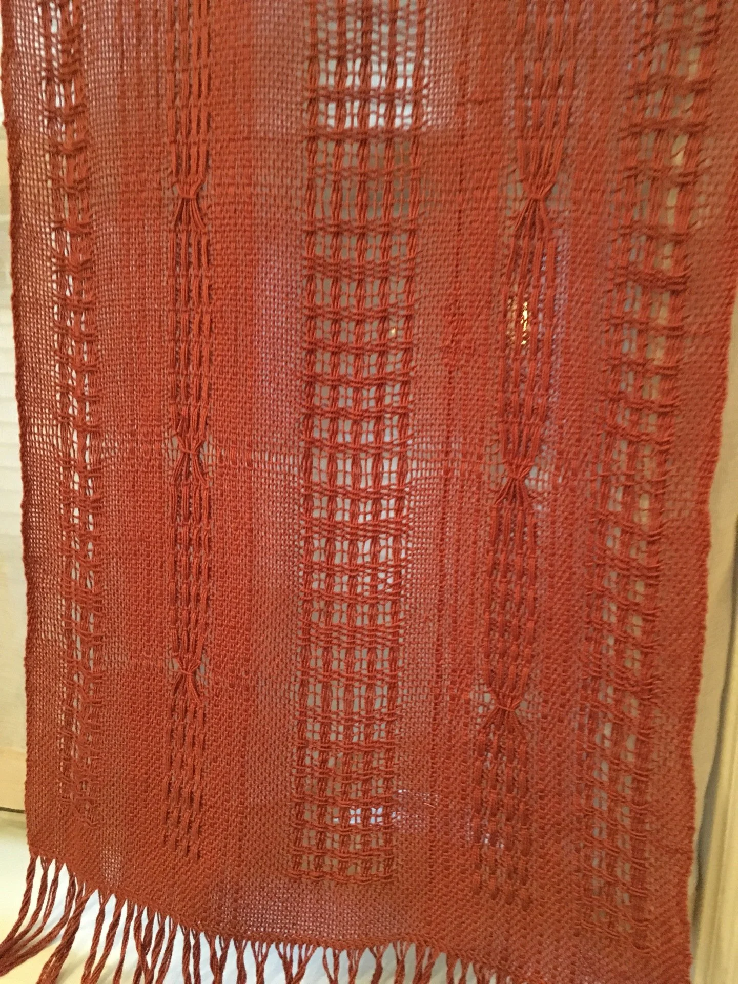 A close-up of a red, woven fabric with intricate patterns and fringe at the bottom.