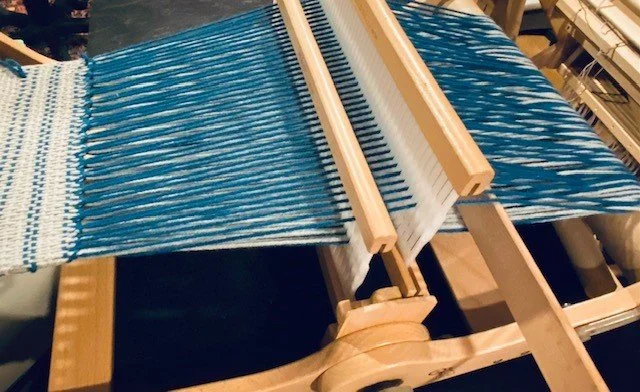 A wooden loom weaving blue and white fabric.