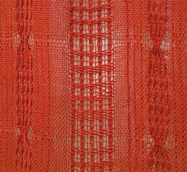 Close-up of orange woven fabric with intricate patterns and open weave in the center.