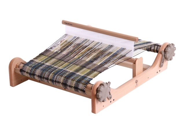 A weaving loom with a partially woven fabric in green, blue, black, and beige colors.