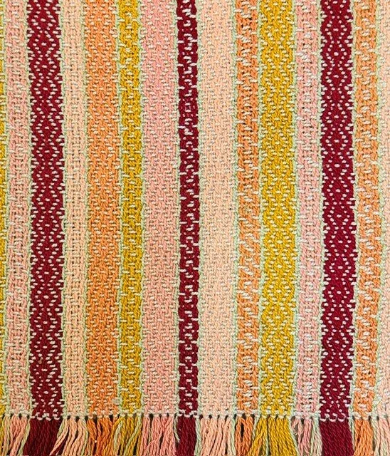 Close-up of a colorful woven or embroidered textile with vertical stripes in red, yellow, pink, orange, and cream.