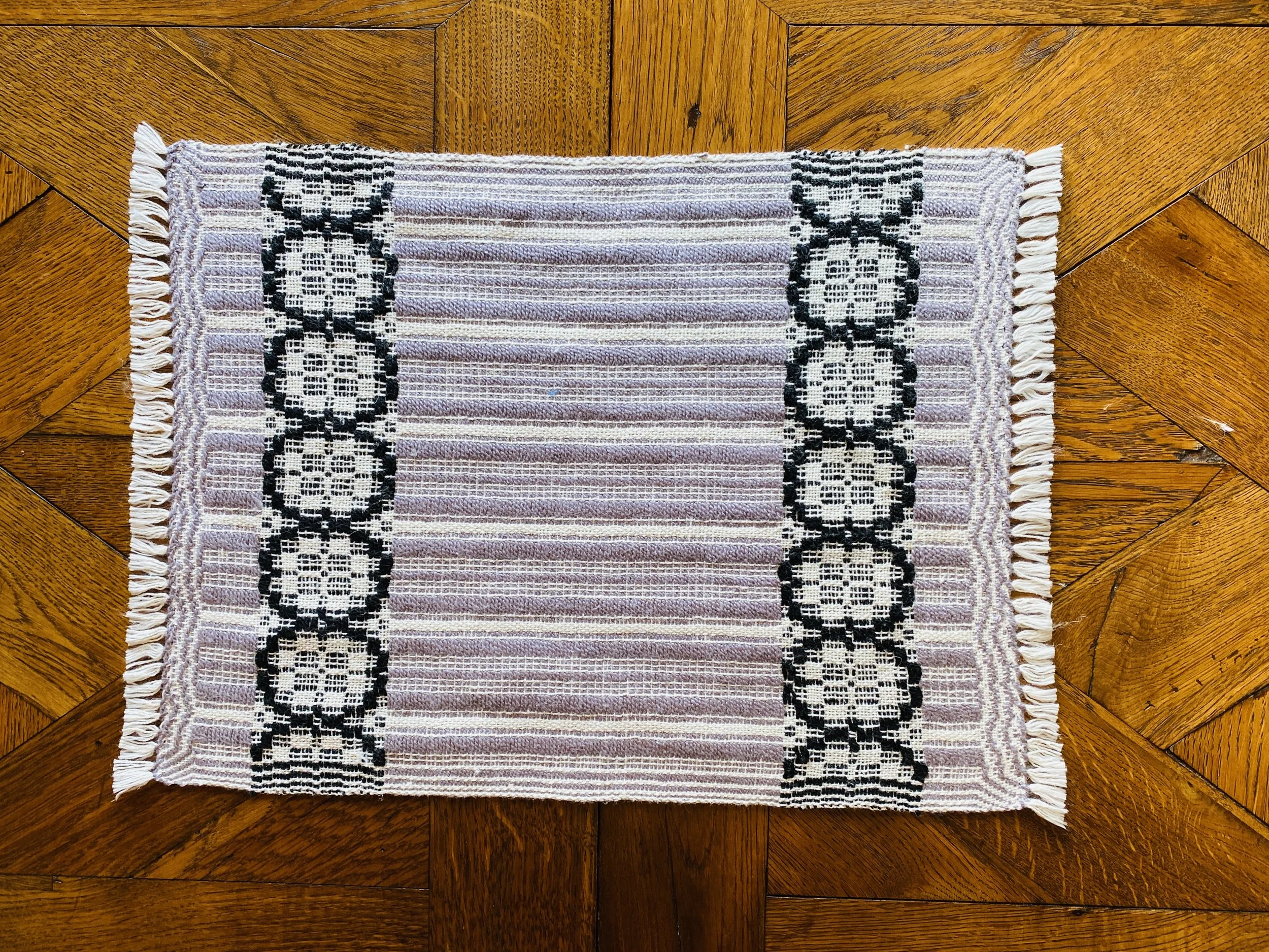 A decorative rug with black and white geometric patterns on a hardwood floor.