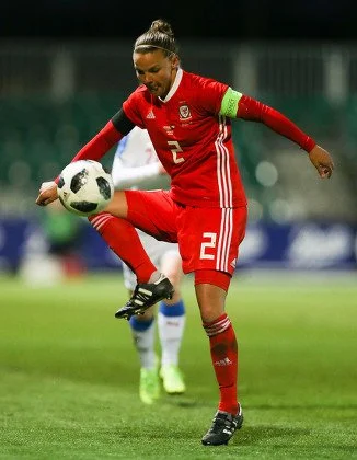 Female soccer player in red uniform with number 21 and green captain's armband, controlling a soccer ball during a match.