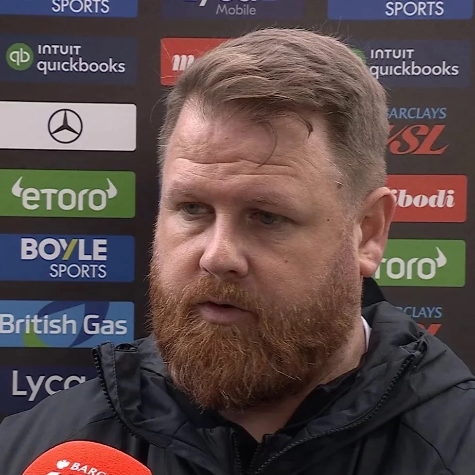 A man with a beard and light brown hair being interviewed, with a backdrop featuring various sponsorship logos including Mercedes, eToro, Boyle Sports, British Gas, and others.