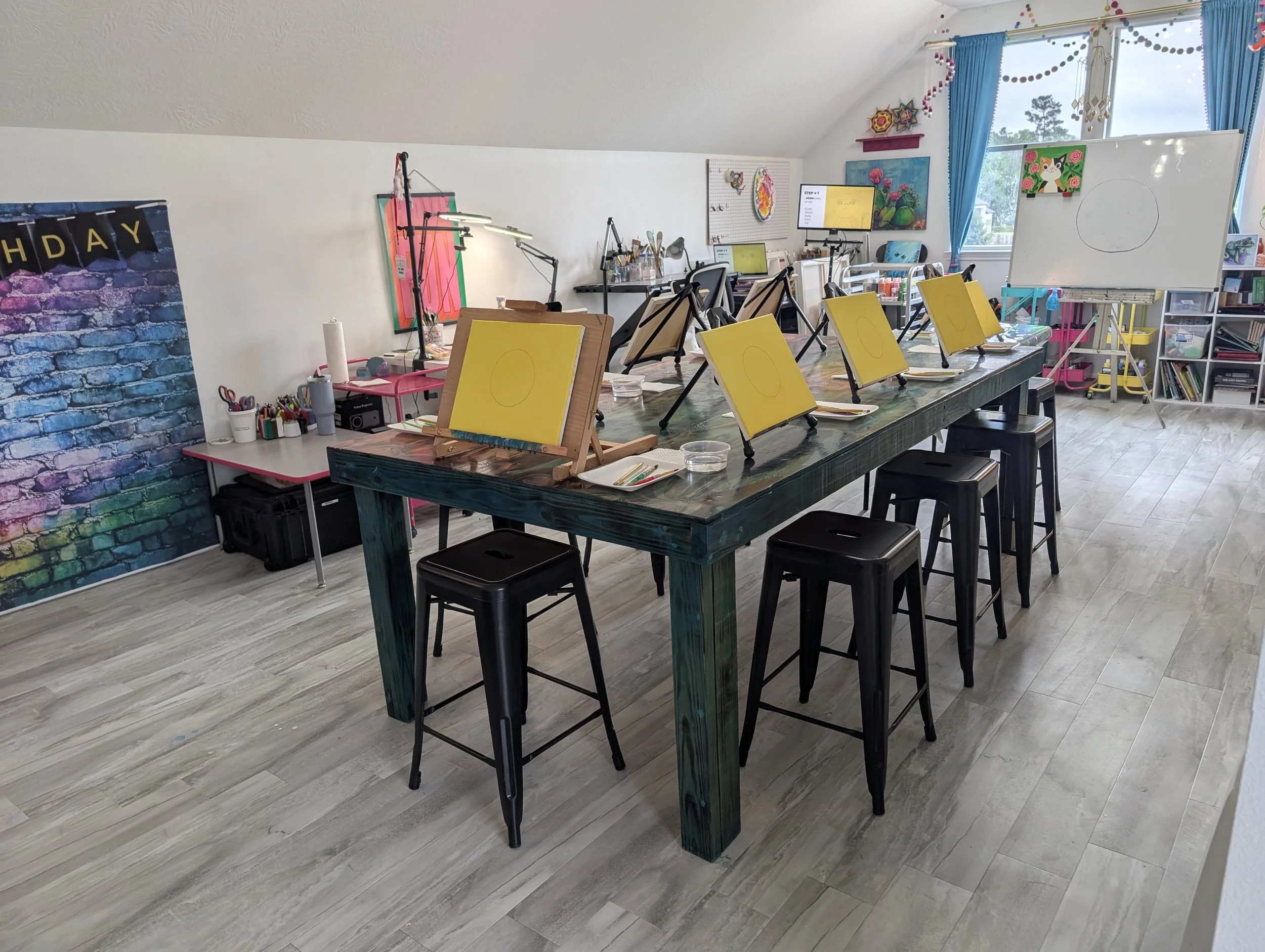 Art workshop or classroom setup with yellow canvases on tables, art supplies, and colorful decorations on the walls and windows.