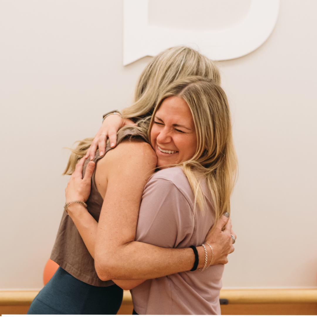 Two women hugging each other embrace warmly, smiling with joy and happiness.