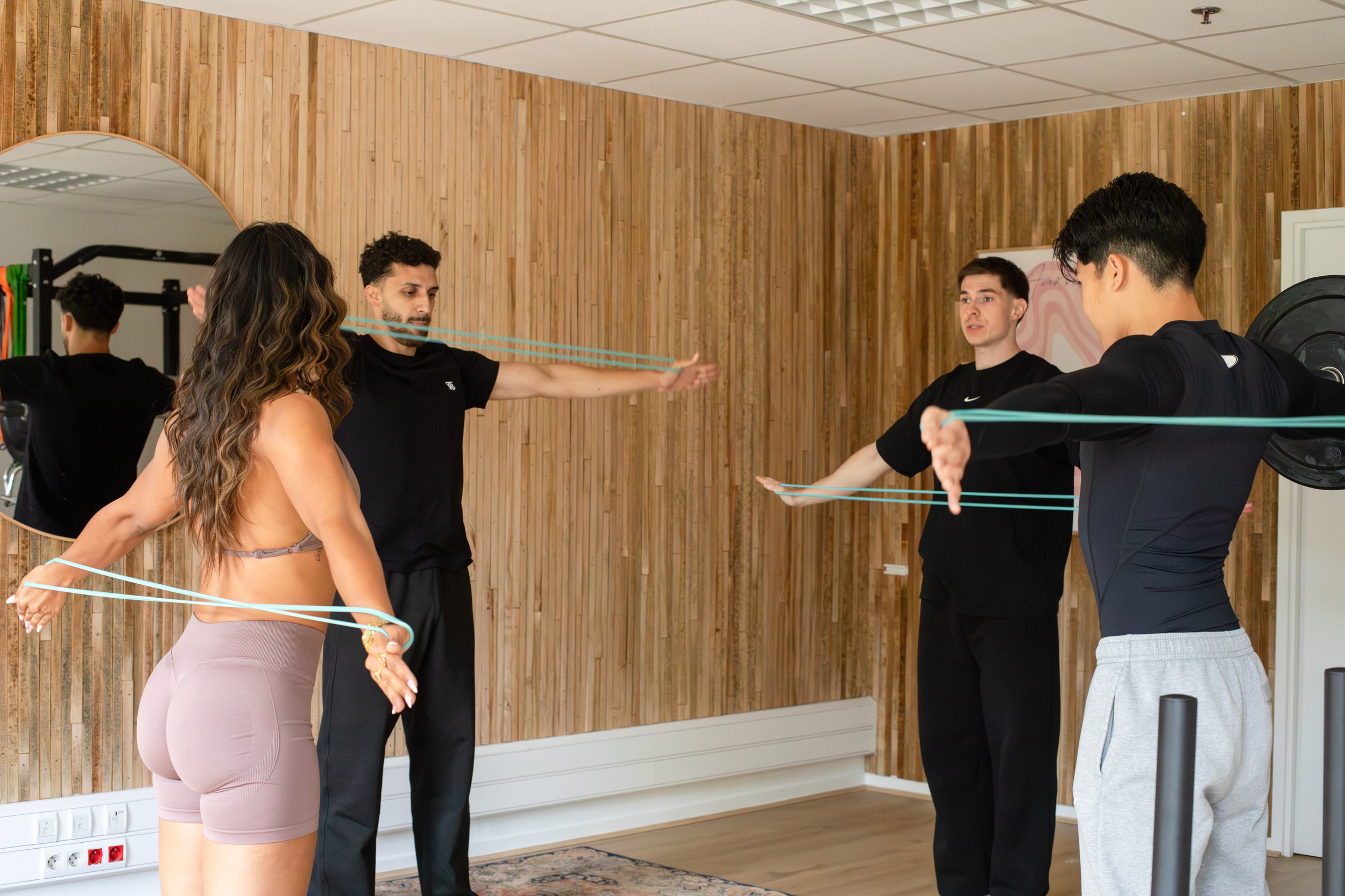 Groupe de personnes en séance de rééducation ou d'exercices avec bandes de résistance dans une salle de sport, membre masculins s'entraînant sous la supervision d'un coach.