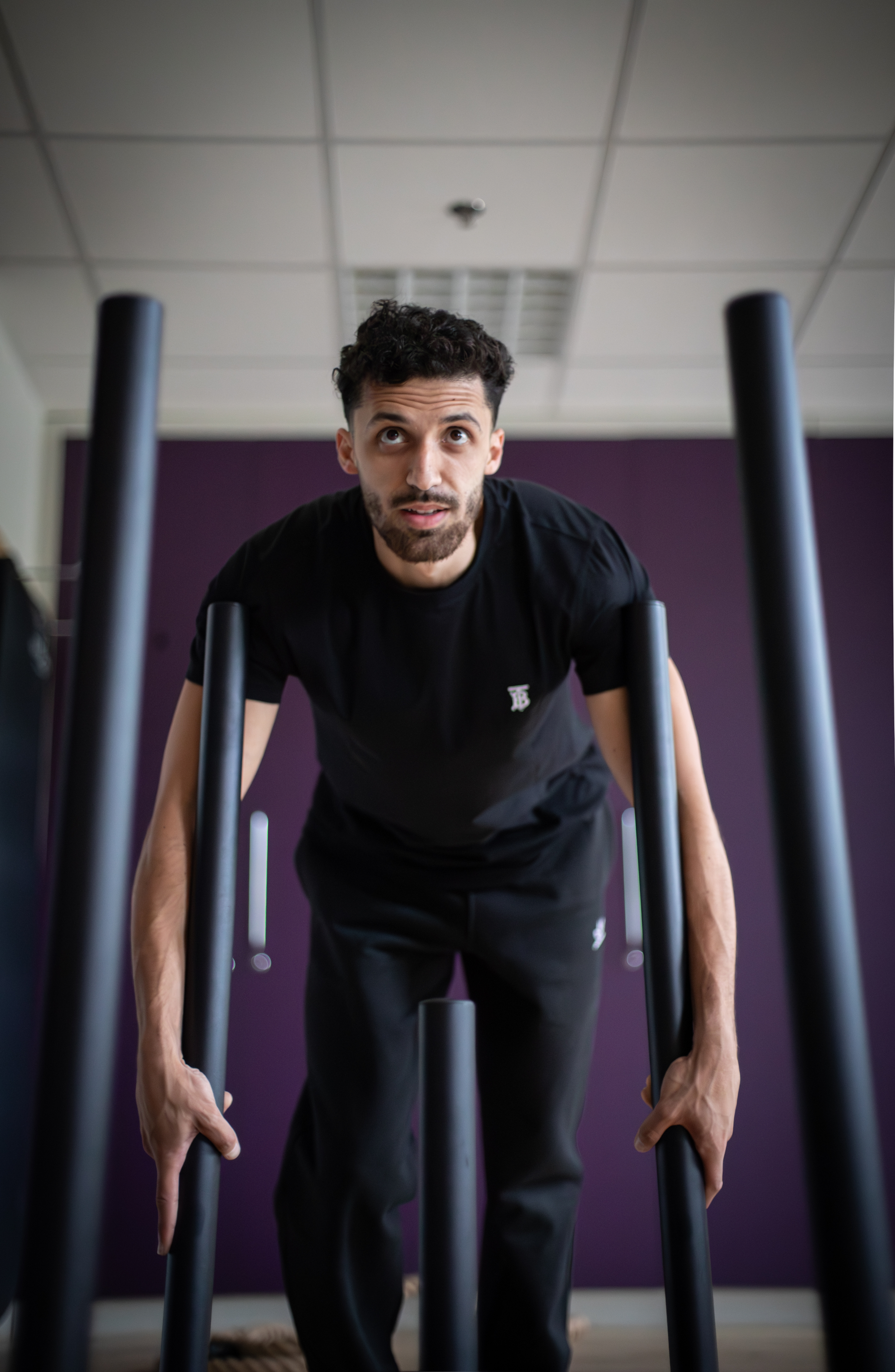 Un homme faisant des flexions à la barre dans une salle de sport avec fond violet.
