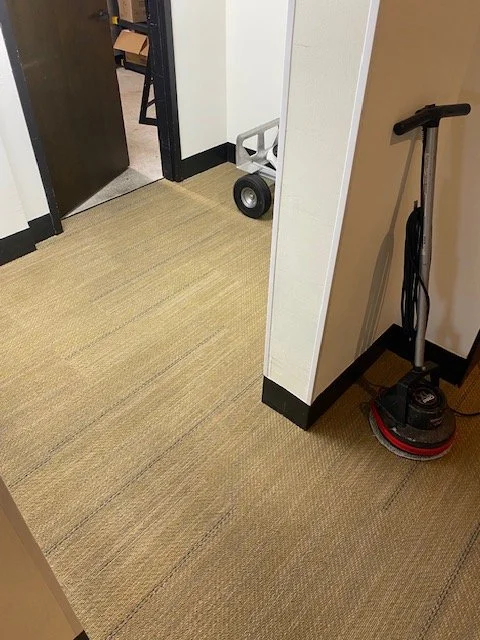 Office hallway corner with a floor cleaning machine and a small cart near the door.