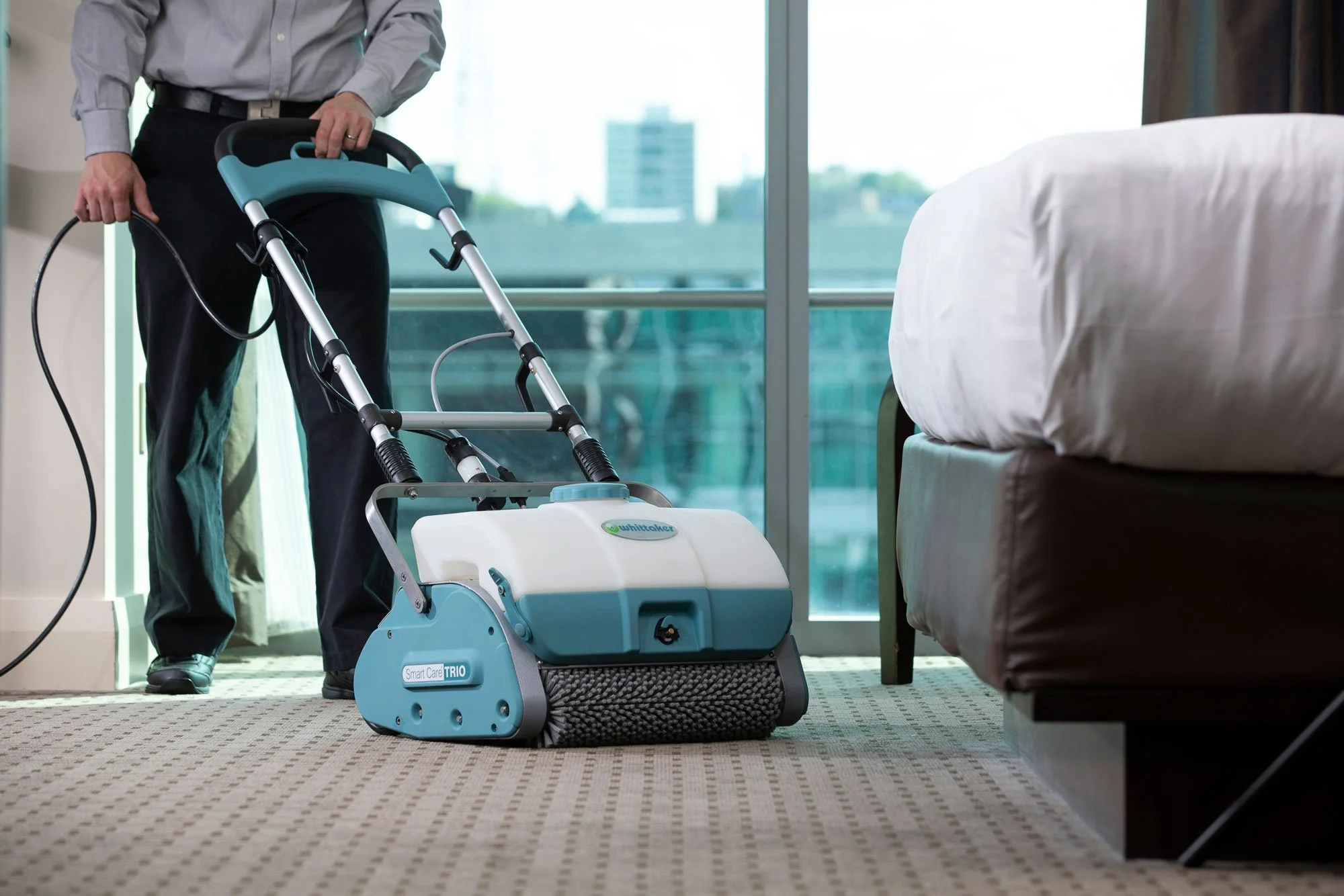 A person using a floor cleaning machine in a hotel room with large windows.