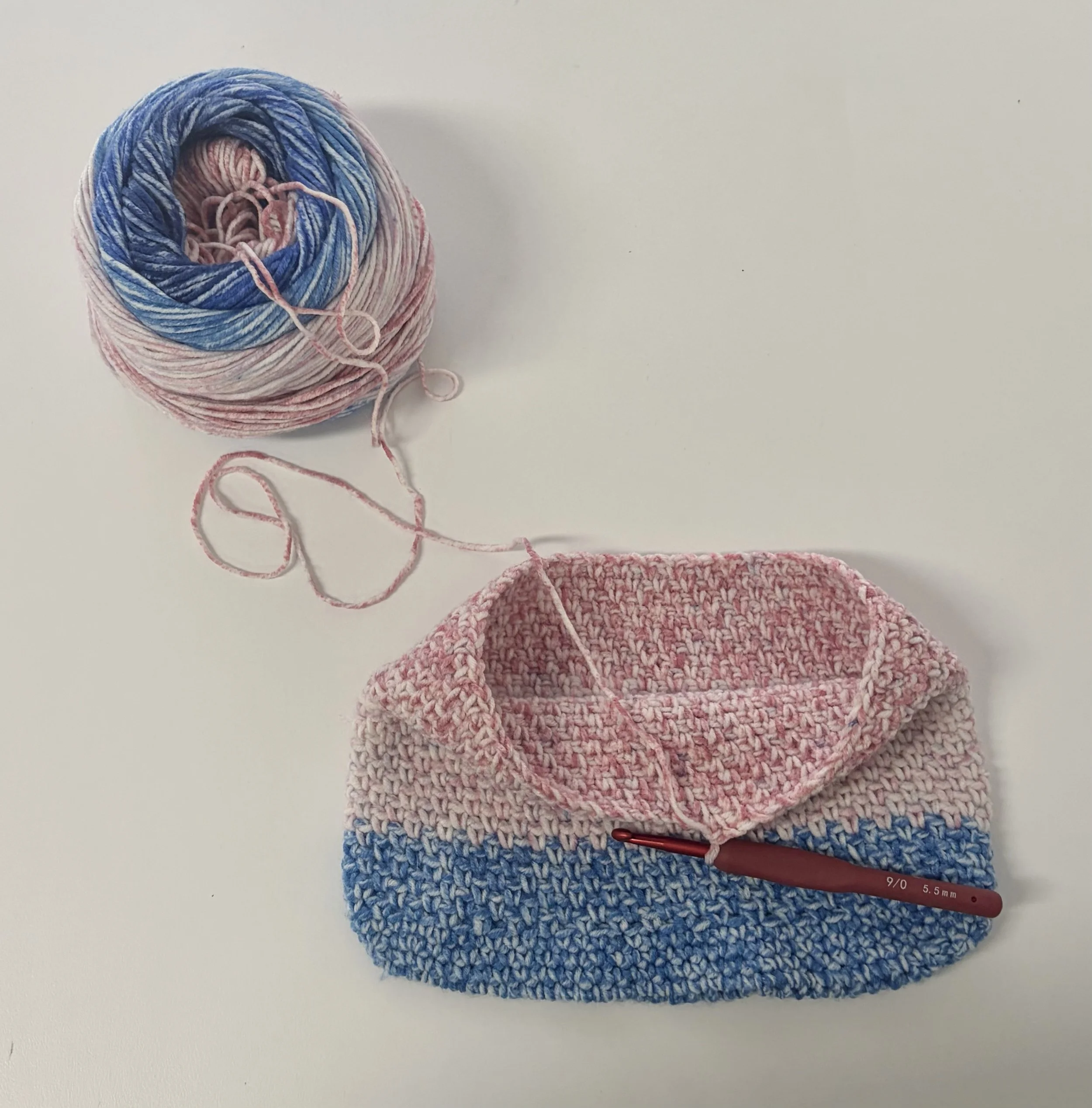 Colorful yarn ball in shades of blue, pink, and white with pink and blue knitting projects in progress on a white surface.