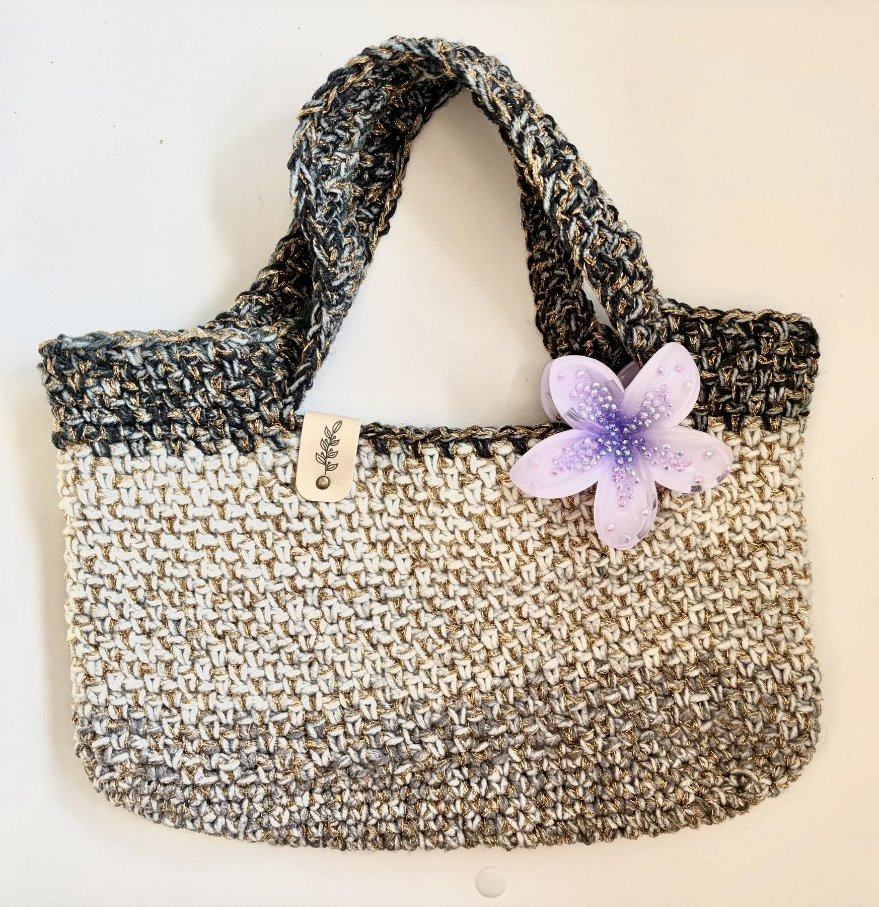A woven handbag with a floral butterfly embellishment and a small tag.