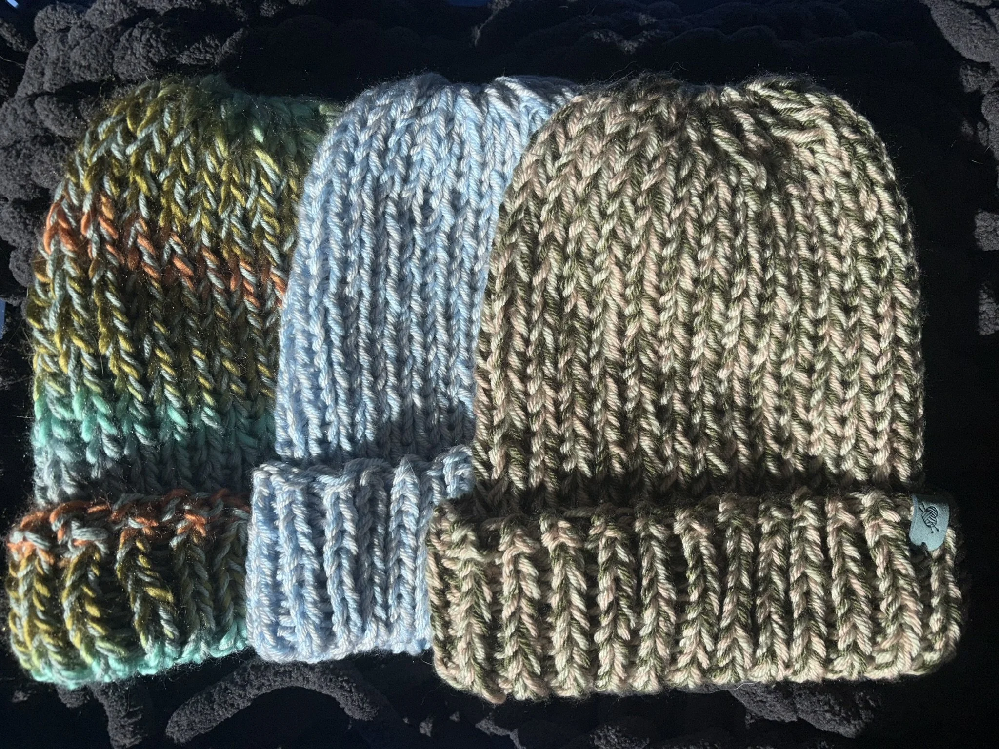 Four knitted beanies in various colors on a black textured surface.