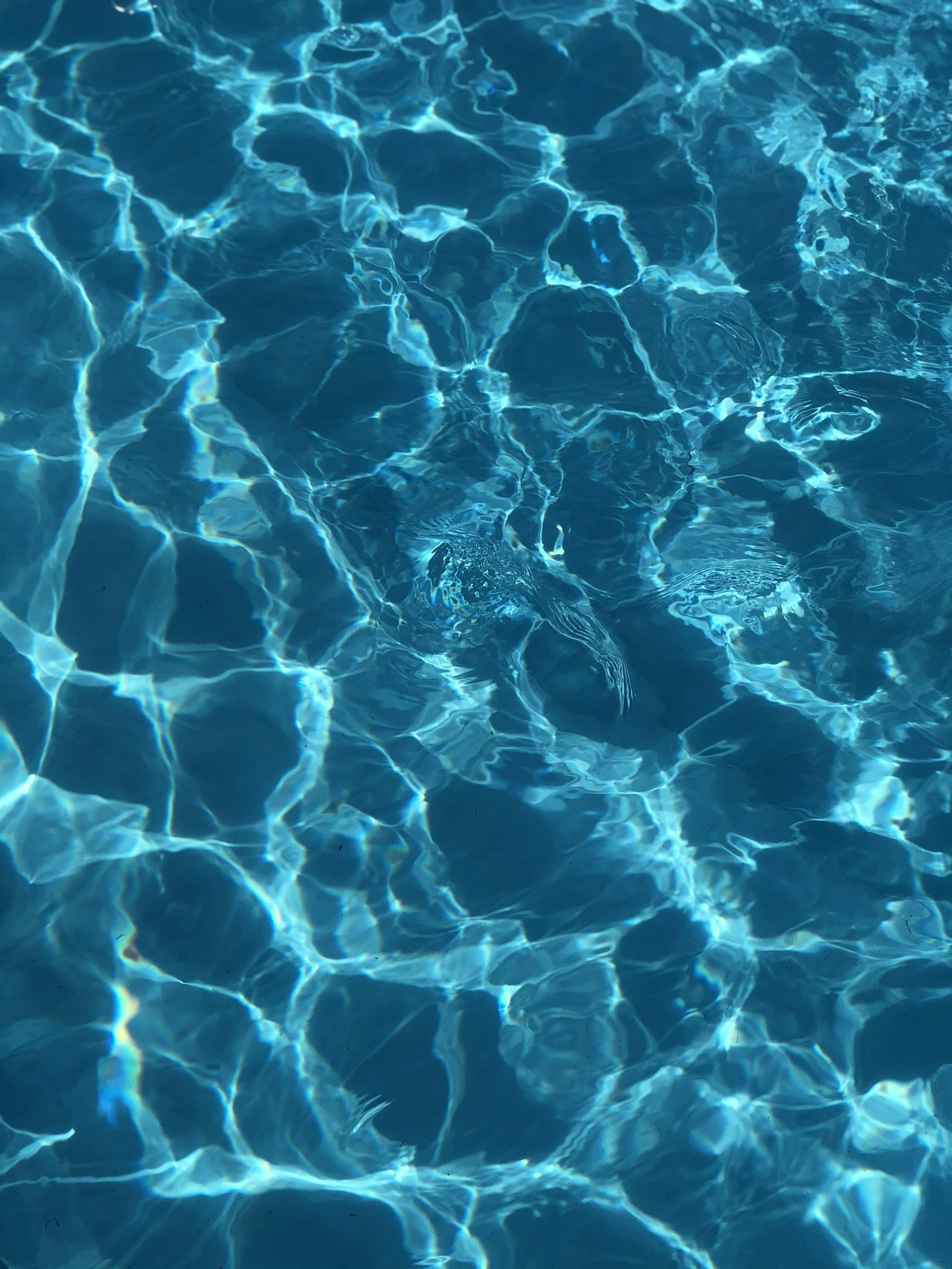 Clear blue swimming pool water with sunlight reflecting off the surface.
