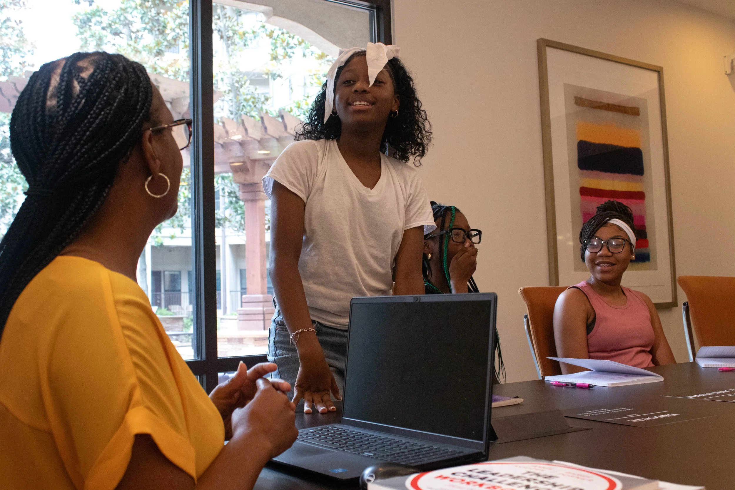A group of women participating in a meeting or discussion in a brightly lit room with large windows and artwork on the walls.