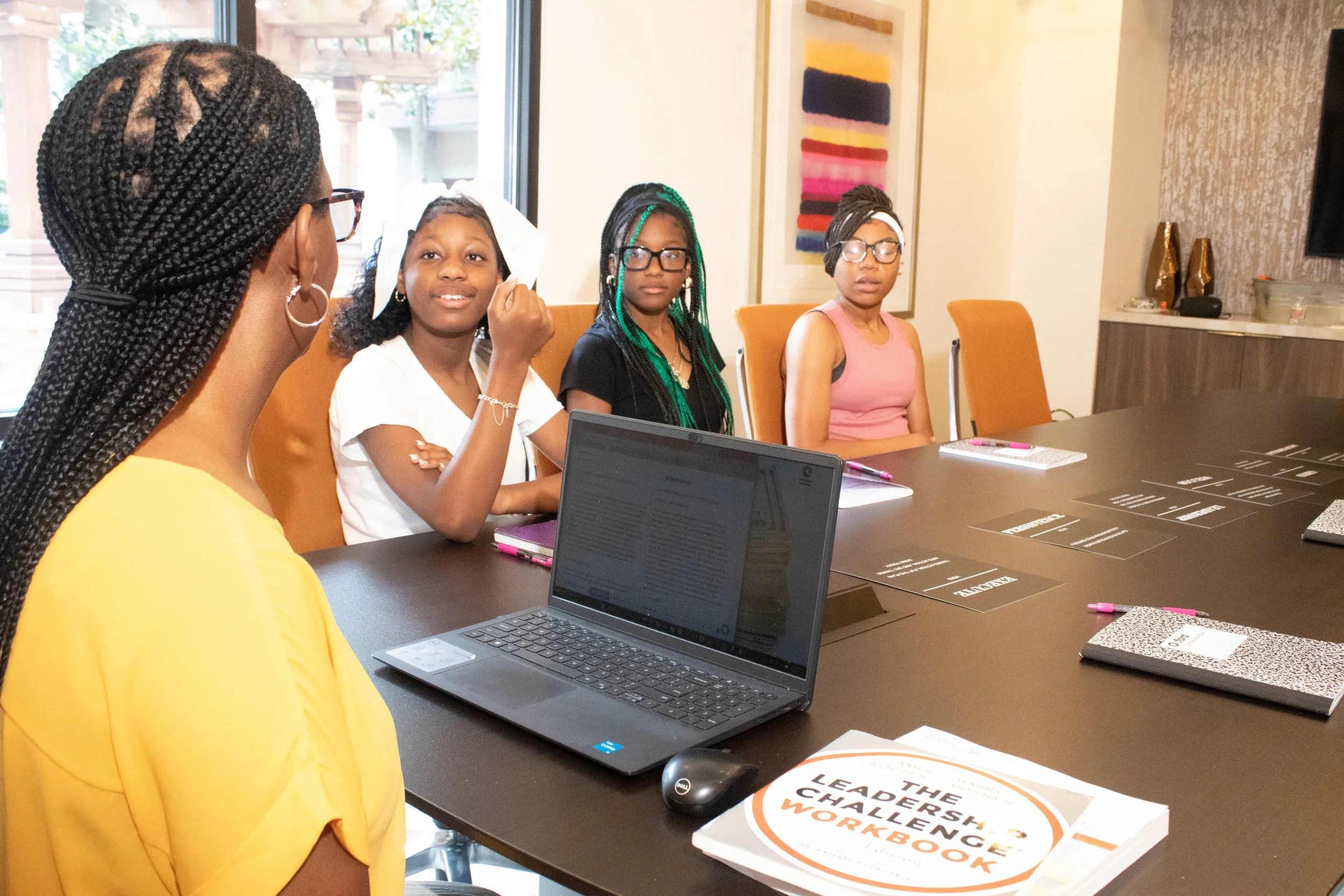 Group of women participating in a workshop or discussion around a table in a conference room, with laptops and notebooks.
