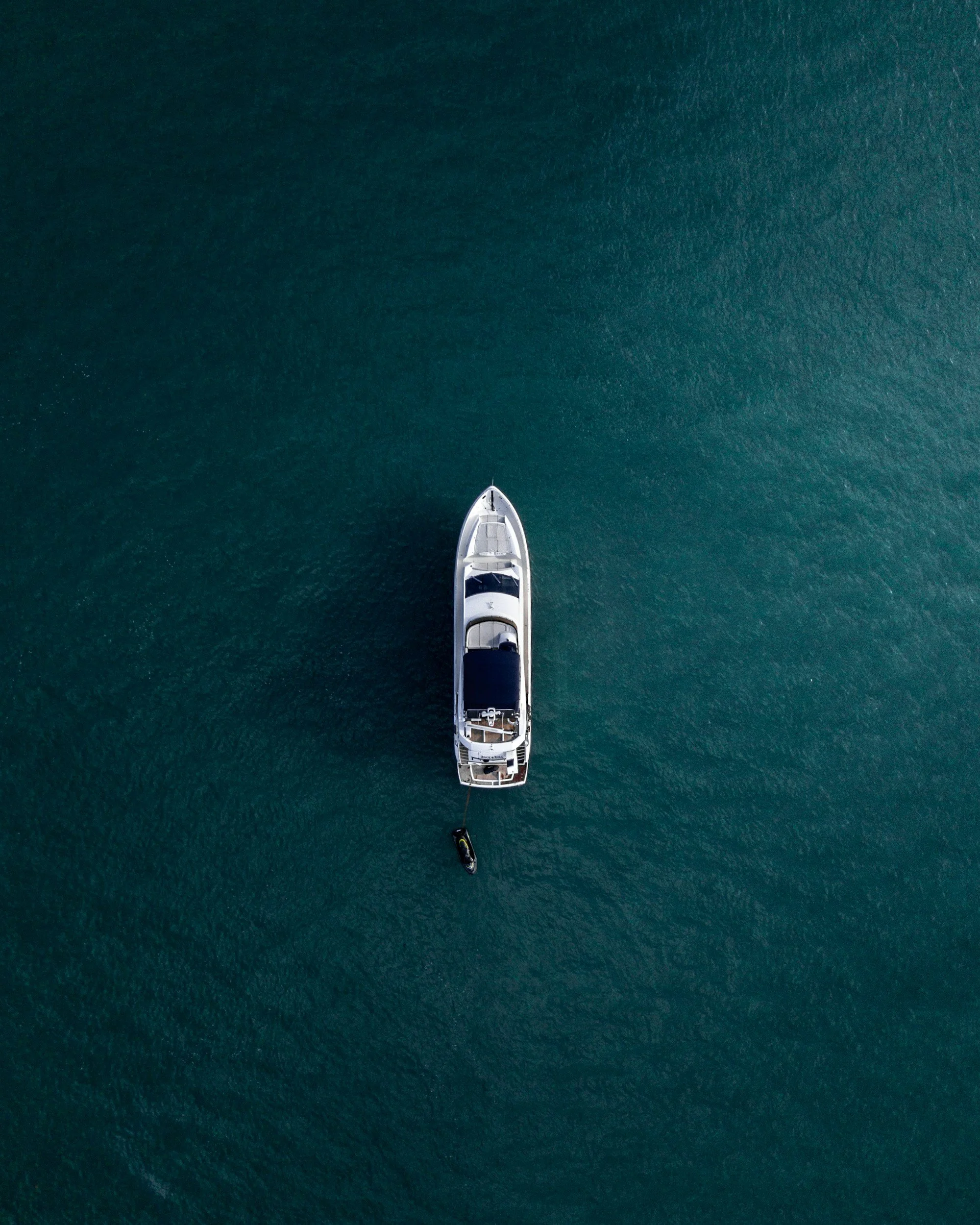 An aerial view of a white yacht and a jet ski on calm, dark green water.