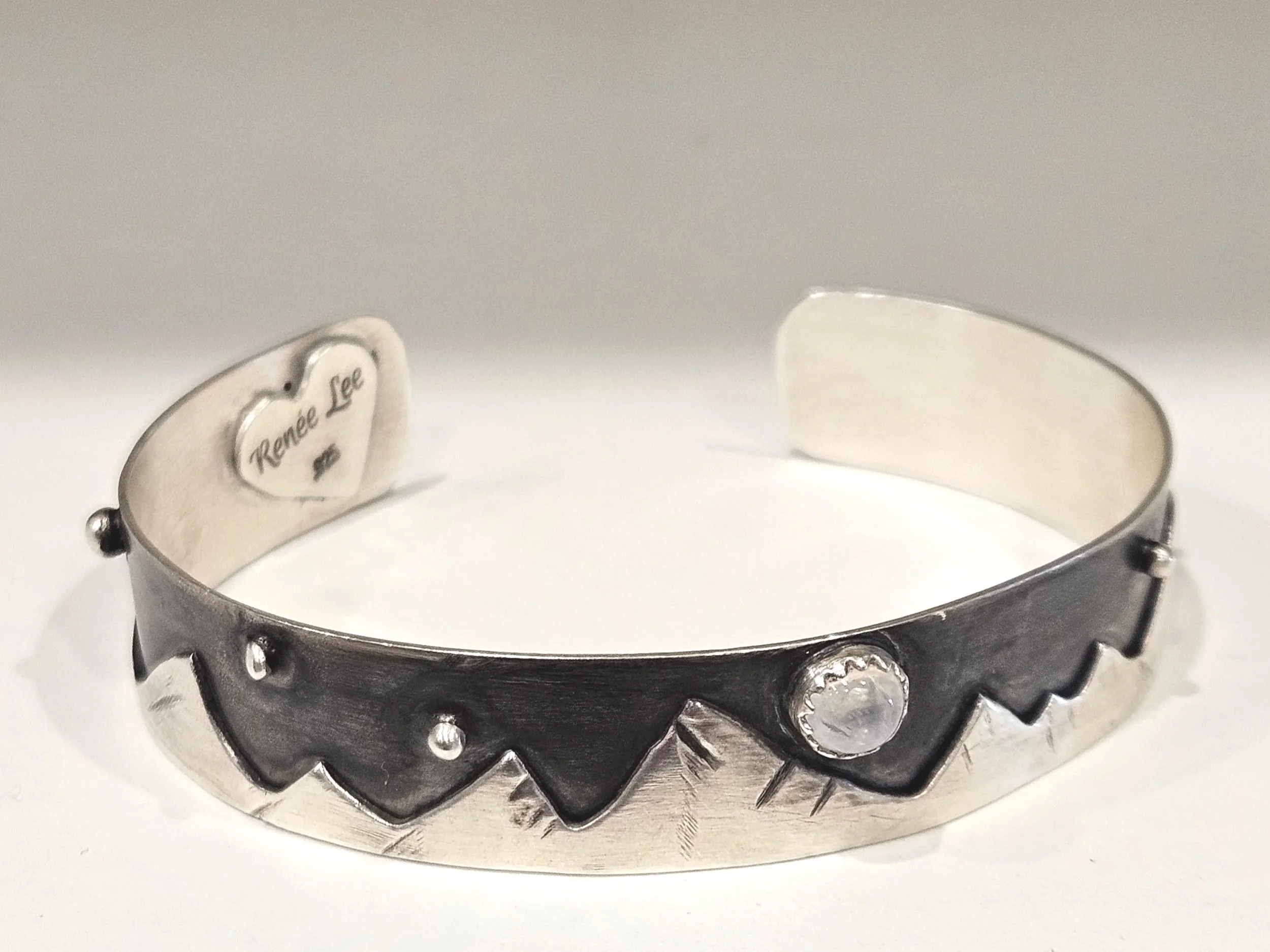Sterling silver night sky and mountain scene cuff bracelet with a rainbow moonstone gemstone.
