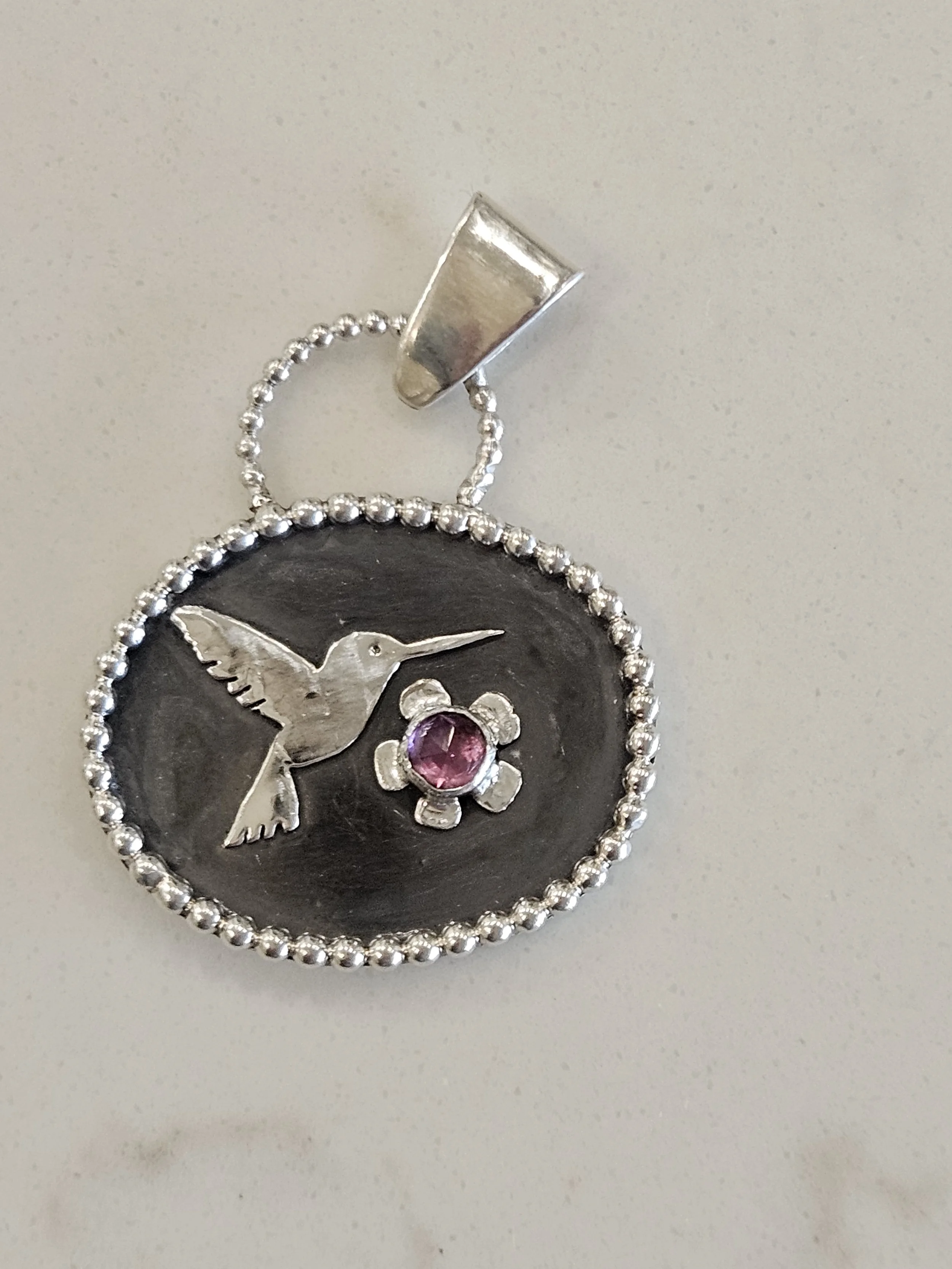 Sterling silver pendant with hummingbird design, Rhodolite garnet gemstone, with a beaded border.
