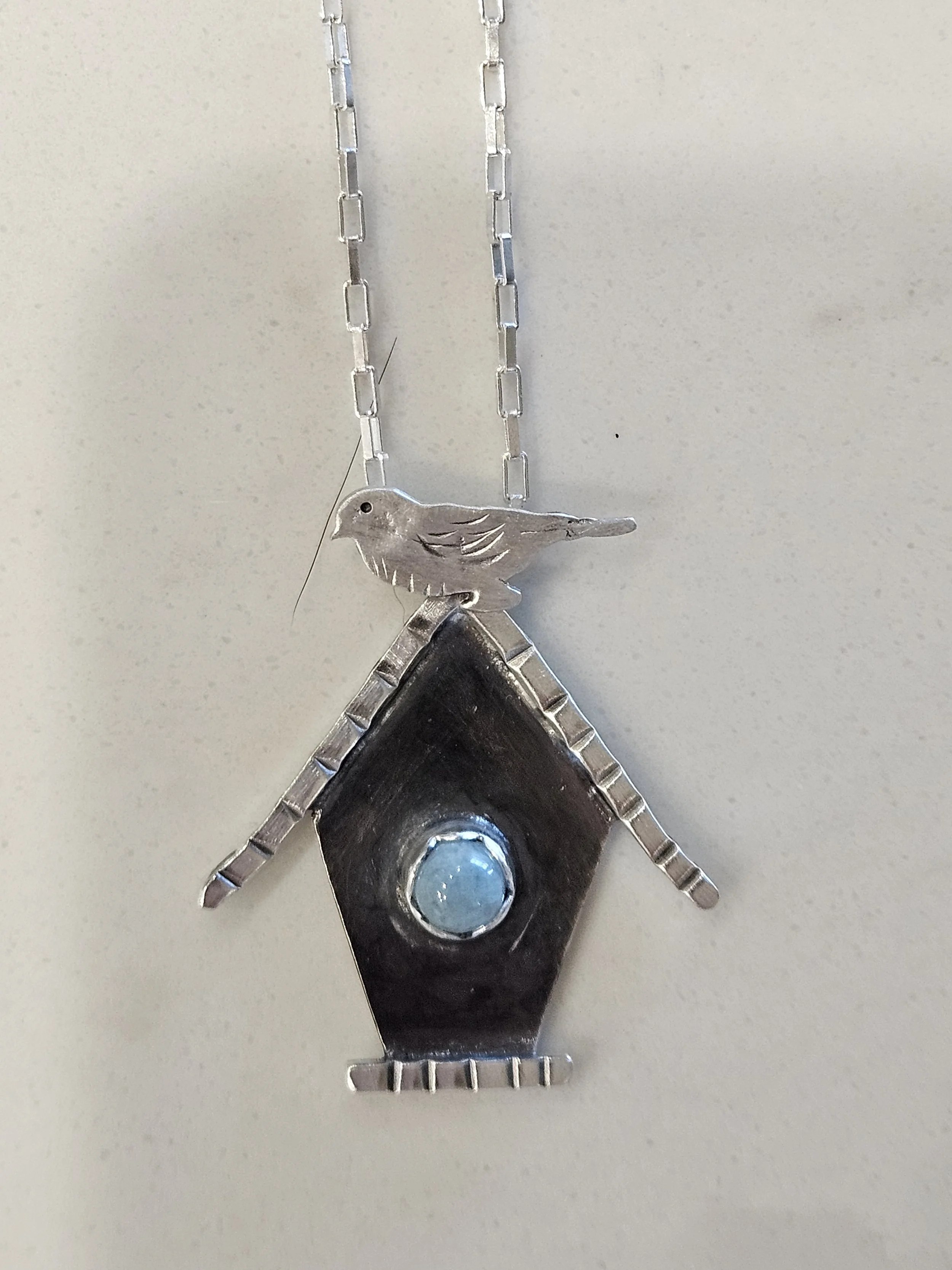Sterling silver birdhouse shaped pendant with an aquamarine gemstone and hidden bail.