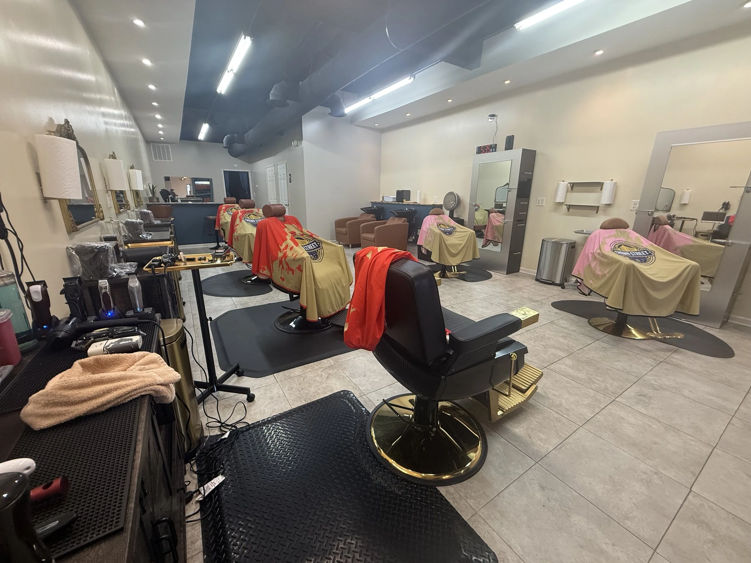 Barber shop with chairs covered in beige cloths, mirrors, and grooming tools, inside a modern salon with bright lighting and tiled floor.