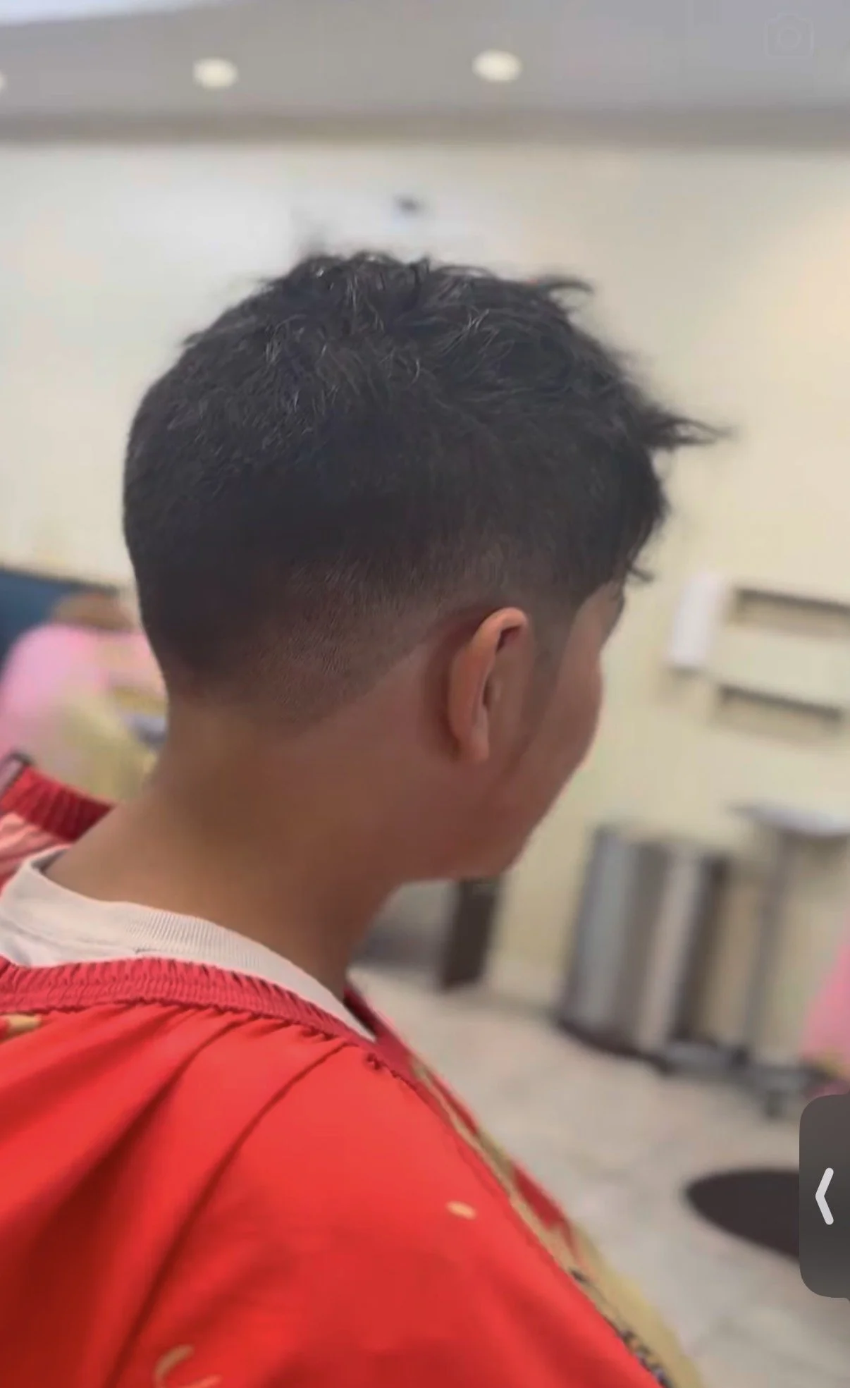 Side view of a young man with a fresh fade haircut, wearing a red jacket, in an indoor setting.
