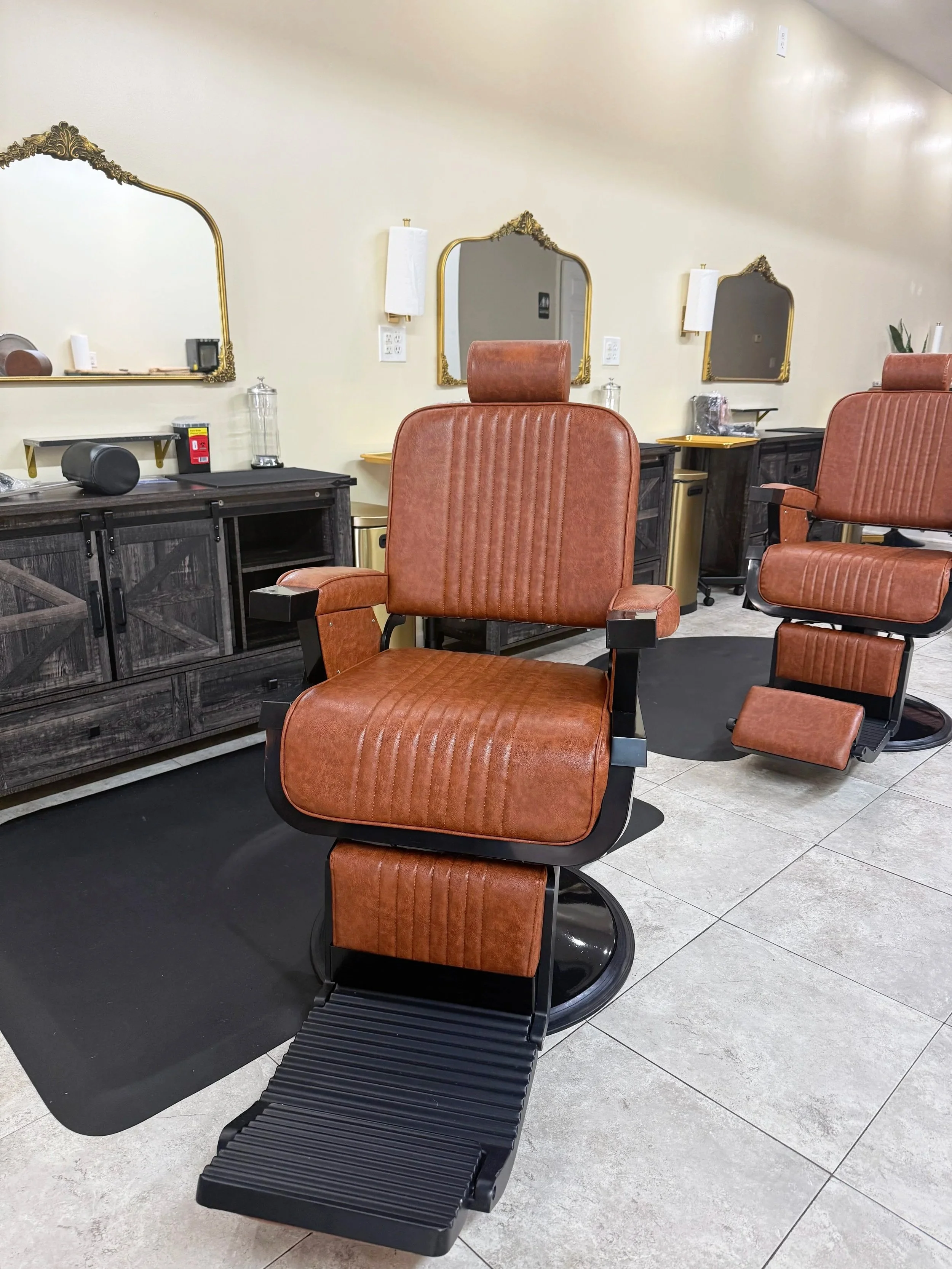 Barber shop with vintage style chairs, large decorative mirrors, and black footrests, set against a light-colored wall with light fixtures.