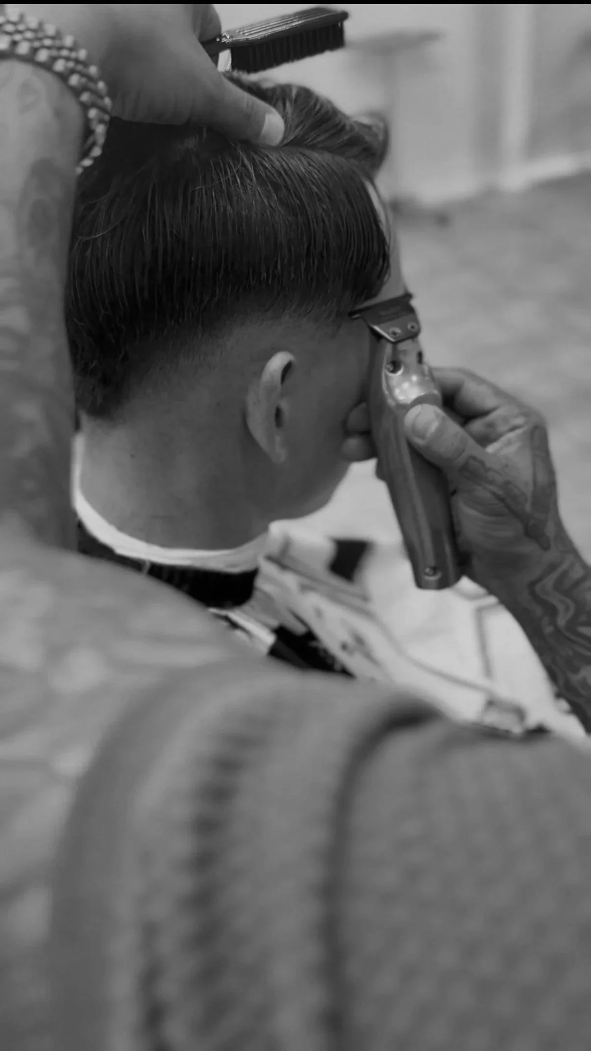 A person getting a haircut with a hair clipper, viewed from the side, in black and white.