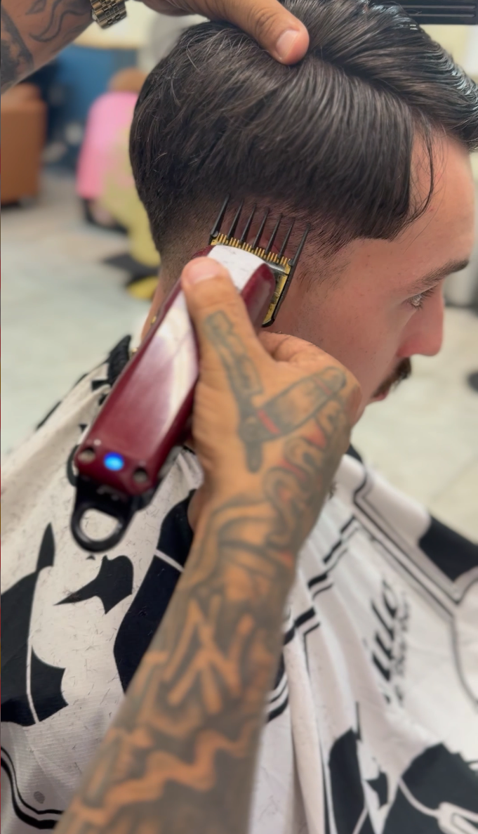Barber trims a man's hair with electric clippers in a barbershop.