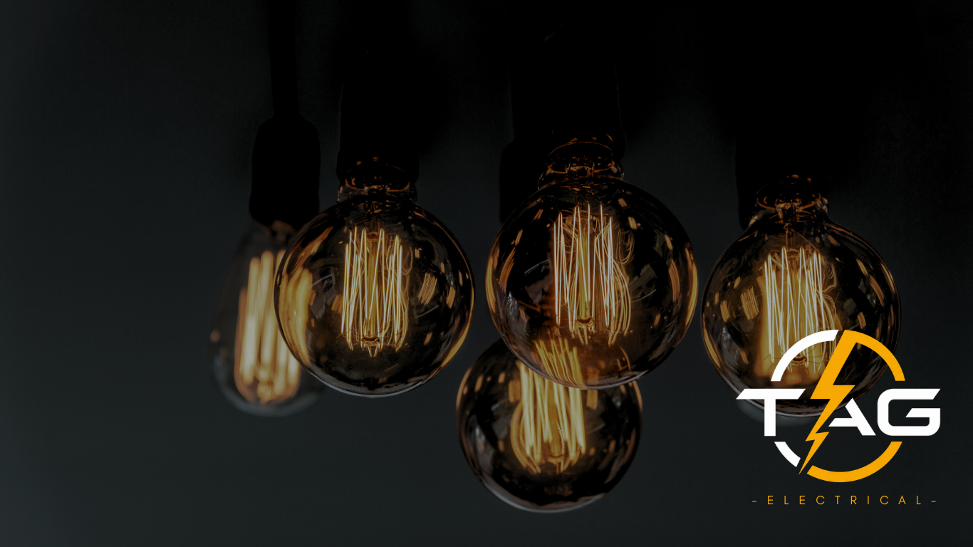 Ceiling light fixture with exposed Edison-style filament bulbs and a logo for TAG Electrical.