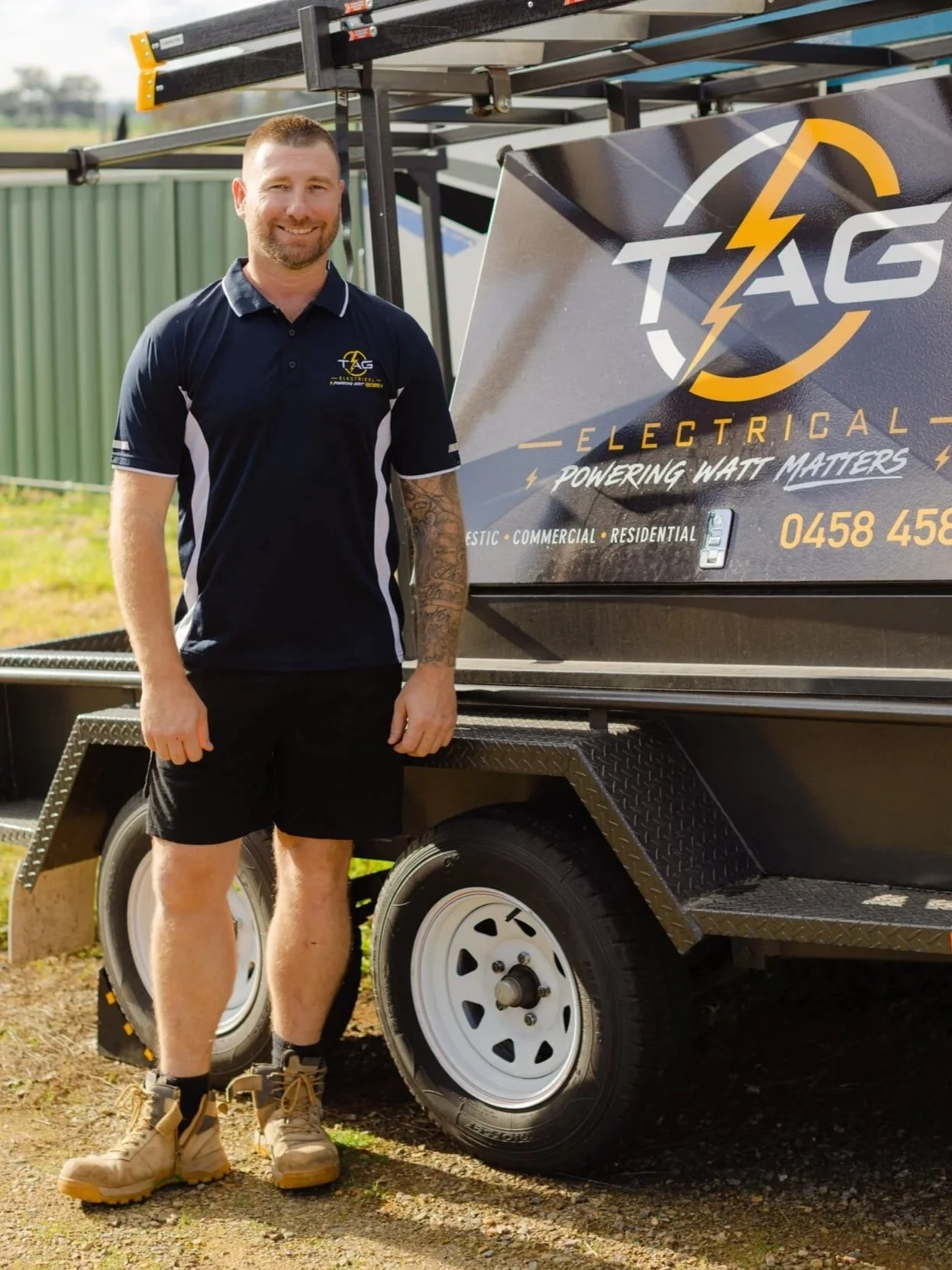 Trusted Wagga Wagga electrician, Trent Garner from TAG Electrical PWM,  standing next to his black utility trailer with TAG Electrical Logo.