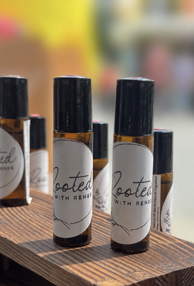 Several small amber glass bottles with black caps labeled "Rooted with Rene" are displayed on a wooden surface, with a blurred colorful background.
