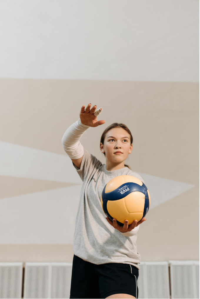 Young woman in sportswear holding a volleyball in an indoor gymnasium.