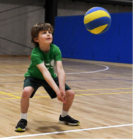 Young boy playing volleyball on an indoor court.