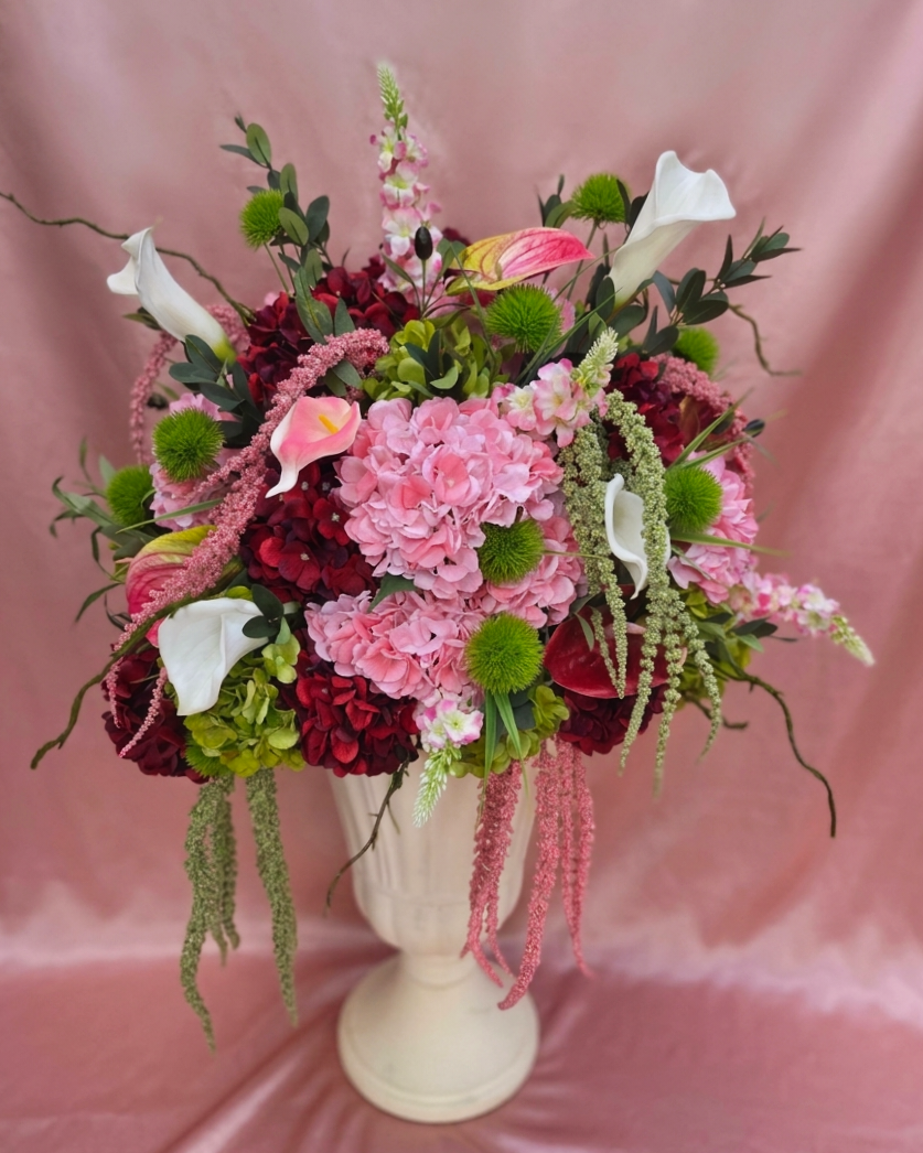 A bouquet of pink, red, white, and green flowers in a white vase, set against a pink background.