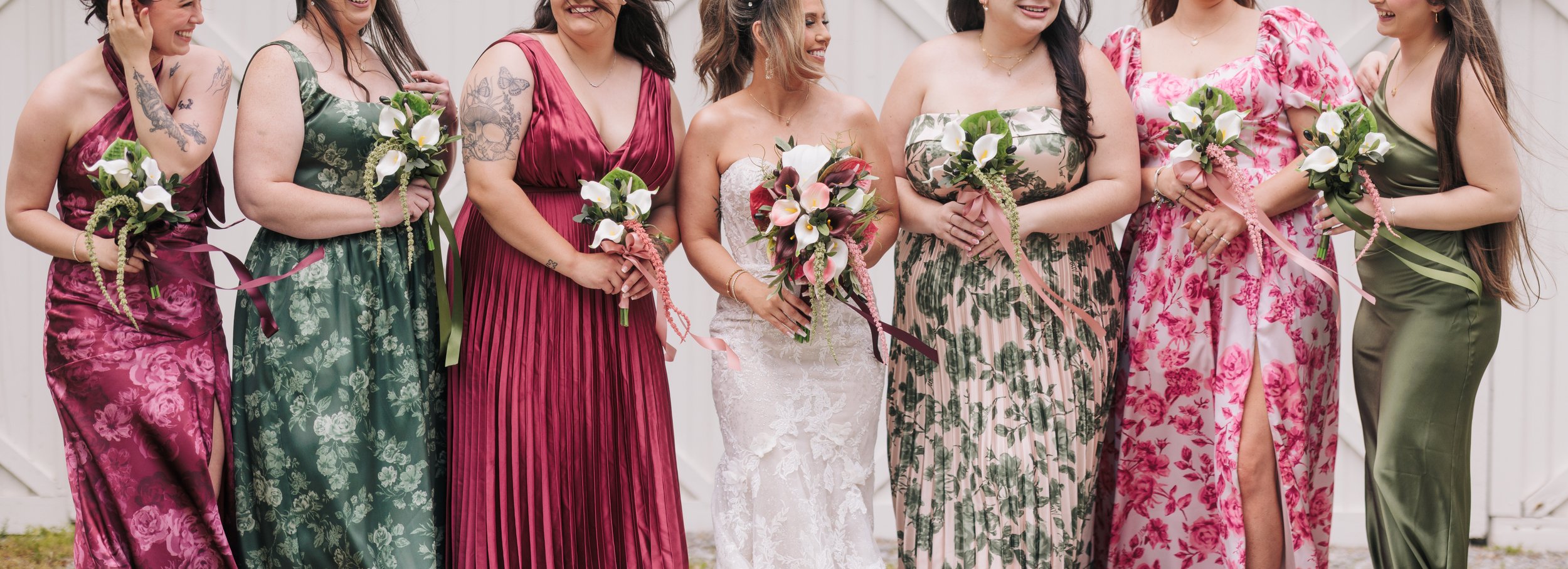 A group of women dressed in colorful, elegant dresses holding bouquets of flowers, posing together at a wedding.