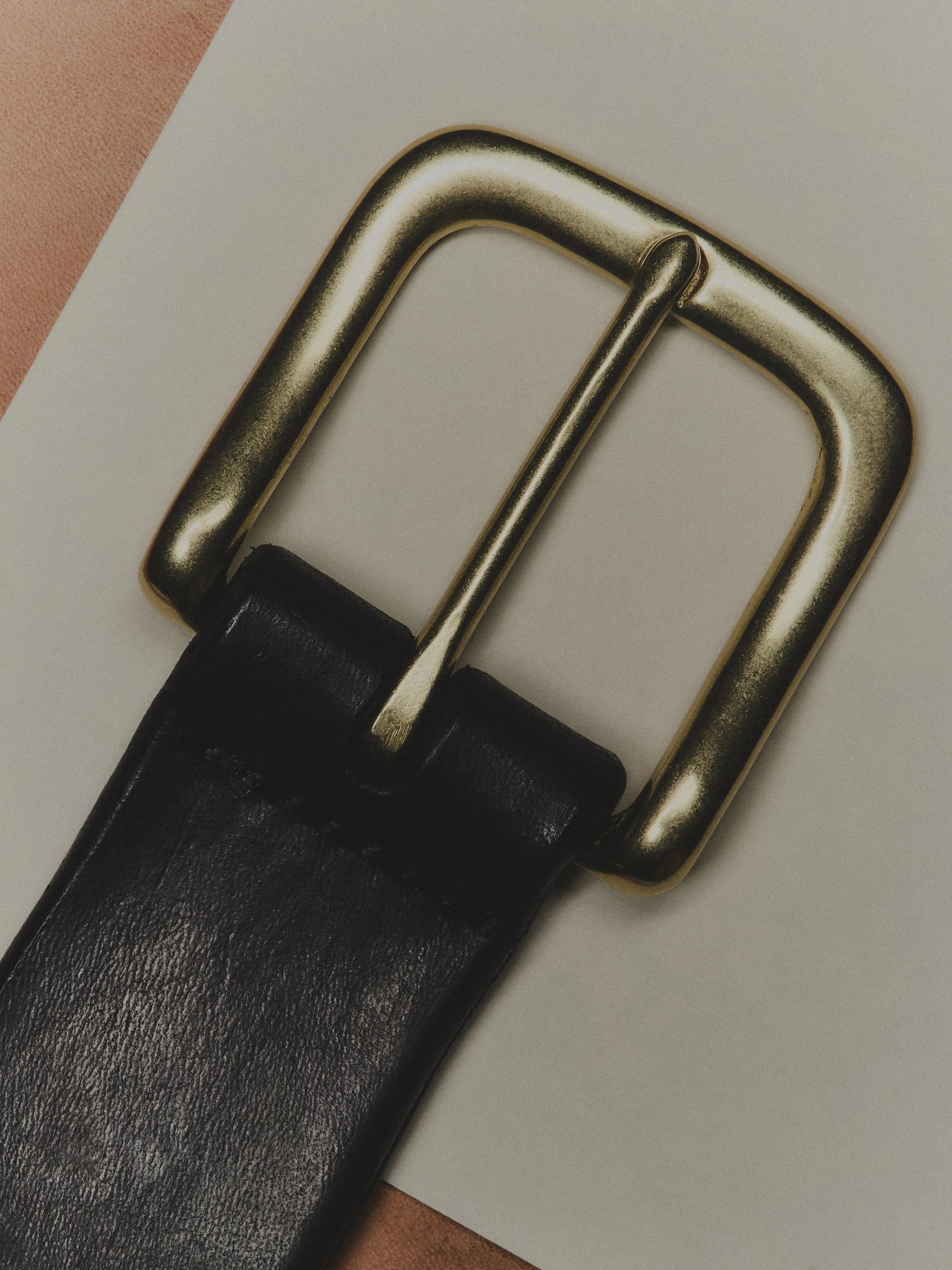 Close-up of a black leather belt with a gold rectangular buckle on a white surface.