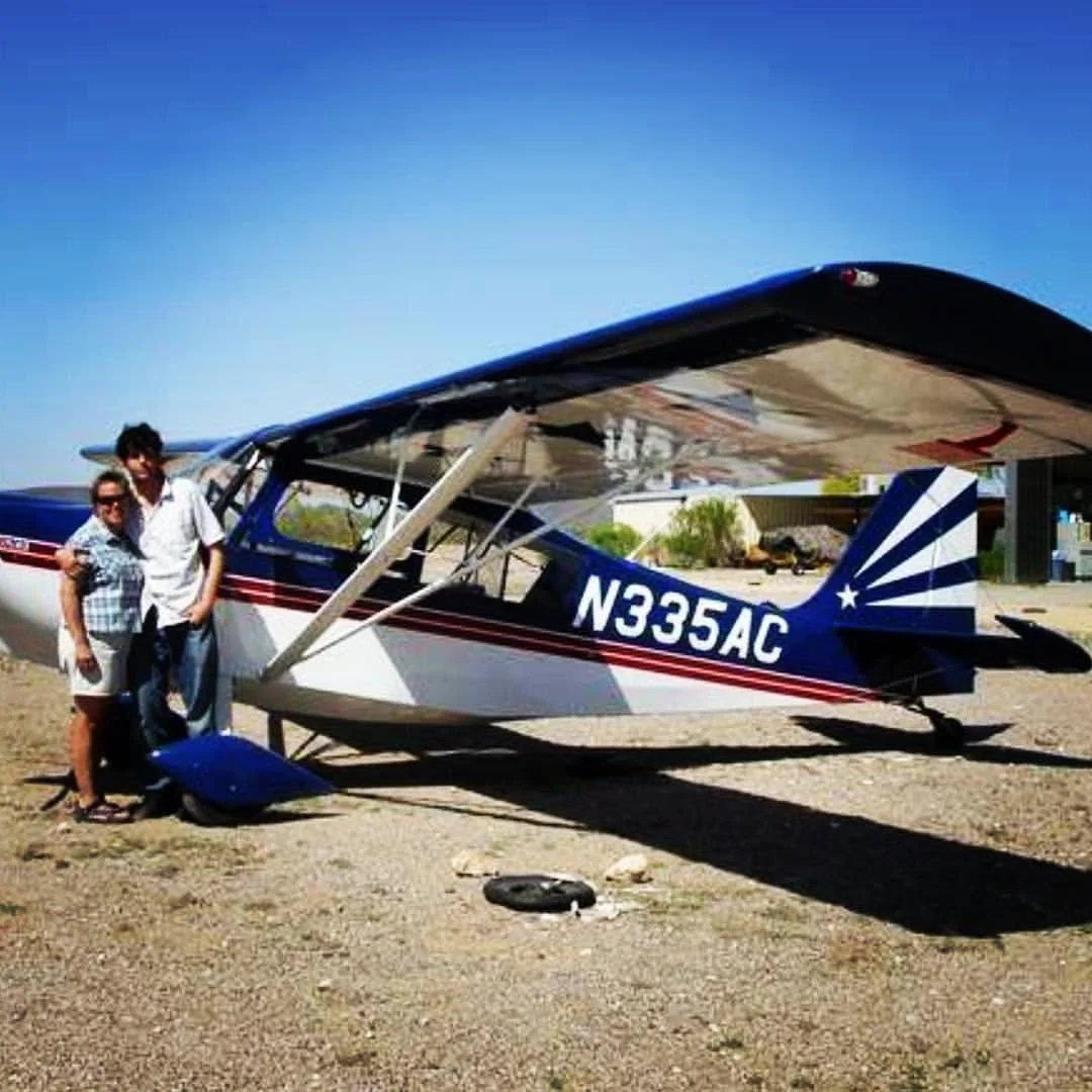 Max Schwartz posing for a photo beside a single-engine aerobatic airplane, called a "Citabria" -- with a white, blue, and red design parked on a gravel area under a clear blue sky. N33AC was a 7GCBC model, with flaps / aileron spades.