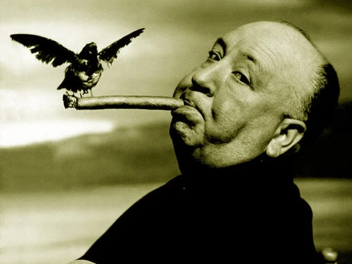 Alfred Hitchcock, with close-cropped hair, has an ironic expression  on his face, as a bird, perched on a stick, appears to be flying or landing near his face. The image is an image to the success of his classic film "The Birds."