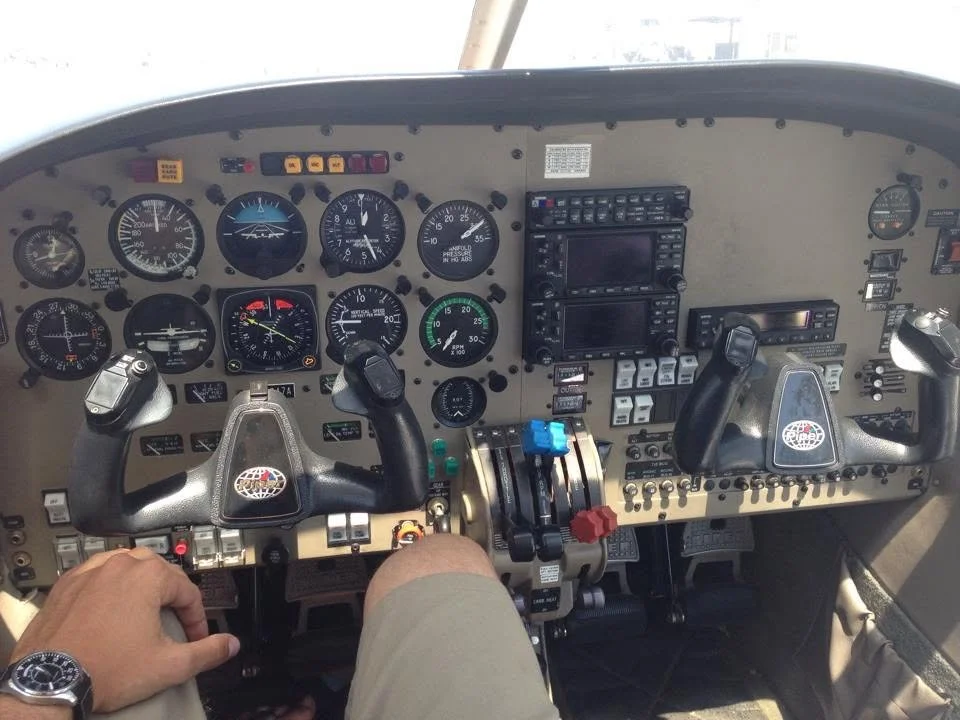 Cockpit of a light twin aircraft, a Piper "Seminole" (PA-44.) Photo shows various gauges, and switches, including two black control yokes, one with a sticker that reads 'AERO'. Interestingly, Piper gives Native American names to their  aircraft.