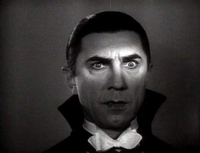 Classic image of Bela Legosi, with his slicked-back hair, wide eyes, and an intense expression. As he plays Dracula, he wears a theatrical costume with a high collar and bow tie. He was a film icon in the horror film world between 1931-1956