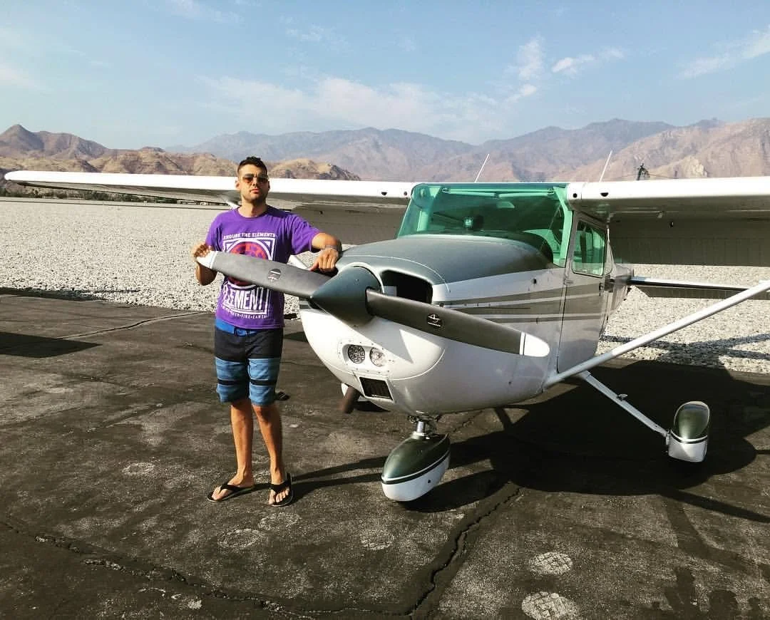 Young man (Max Schwartz) standing near next to a small private airplane, on a tarmac with mountains in the background. Shot in palm Springs. Aircraft was a Cessna 172M. Same model from Bond film "Goldeneye." Tail number was N12749.