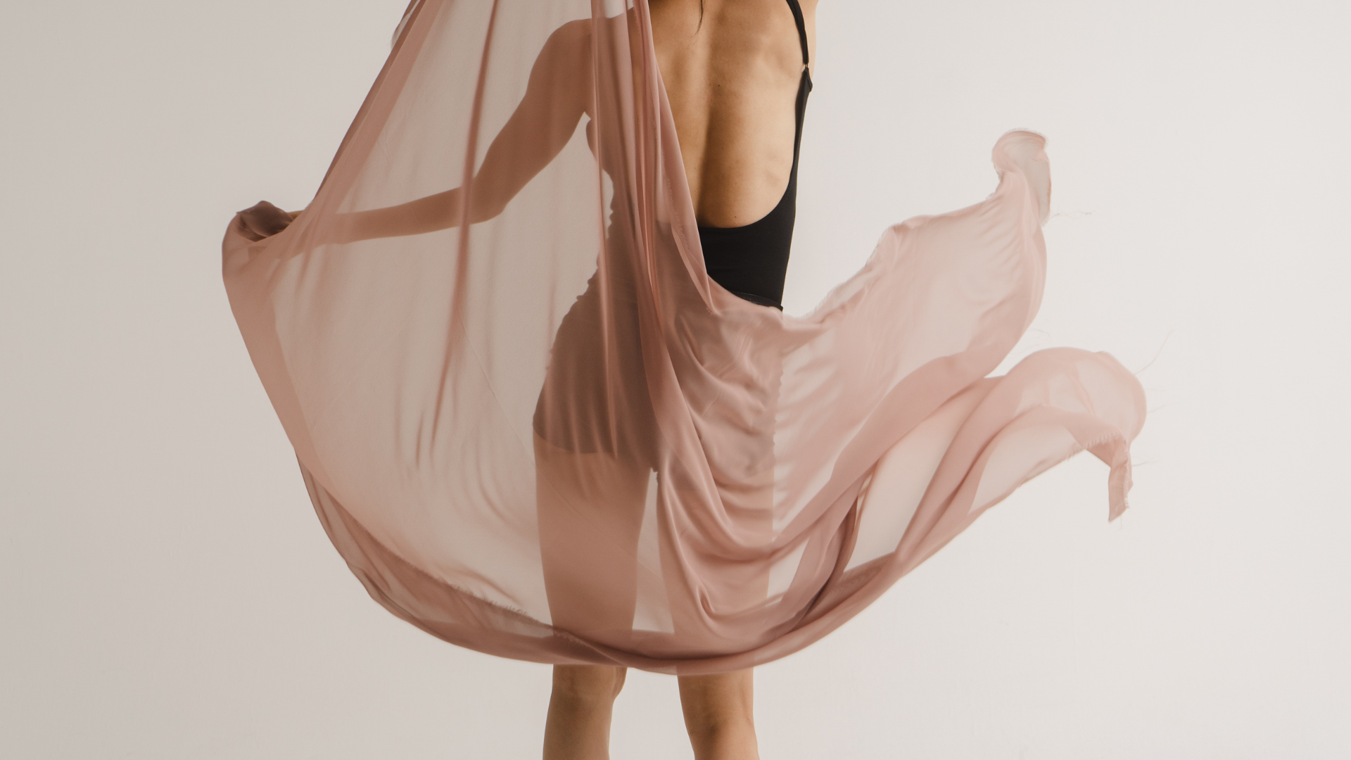 Person dancing or performing with a flowing pink and black dress, captured mid-movement against a plain light background.