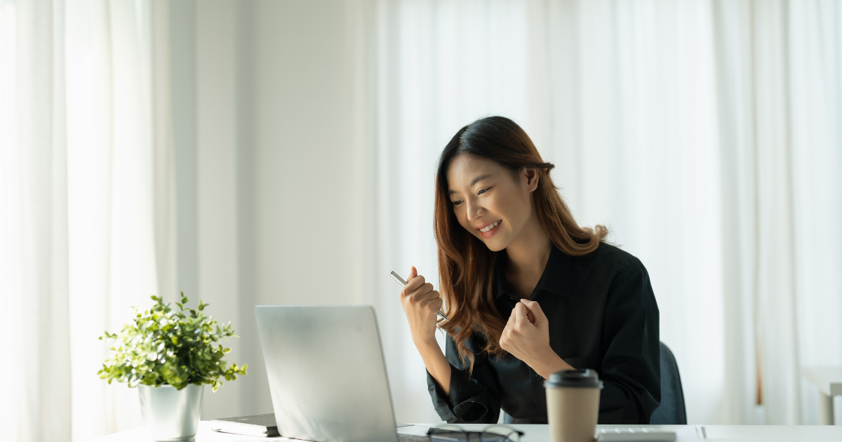 Woman celebrating work success on laptop in bright office