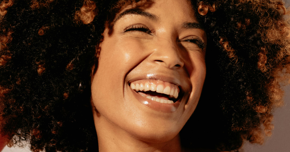 Close-up of a woman with curly hair smiling and laughing.
