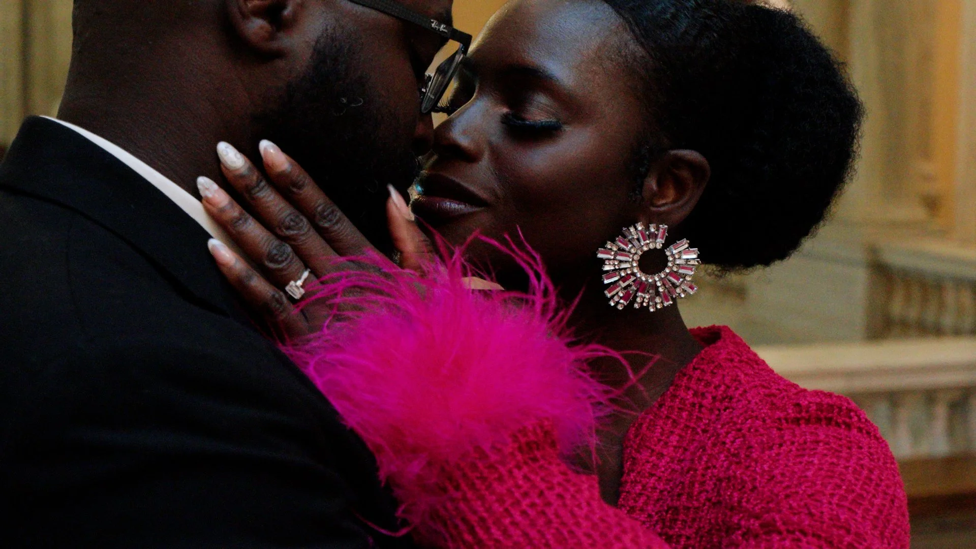 Liam and Moyo are embracing closely, with their faces nearly touching. 