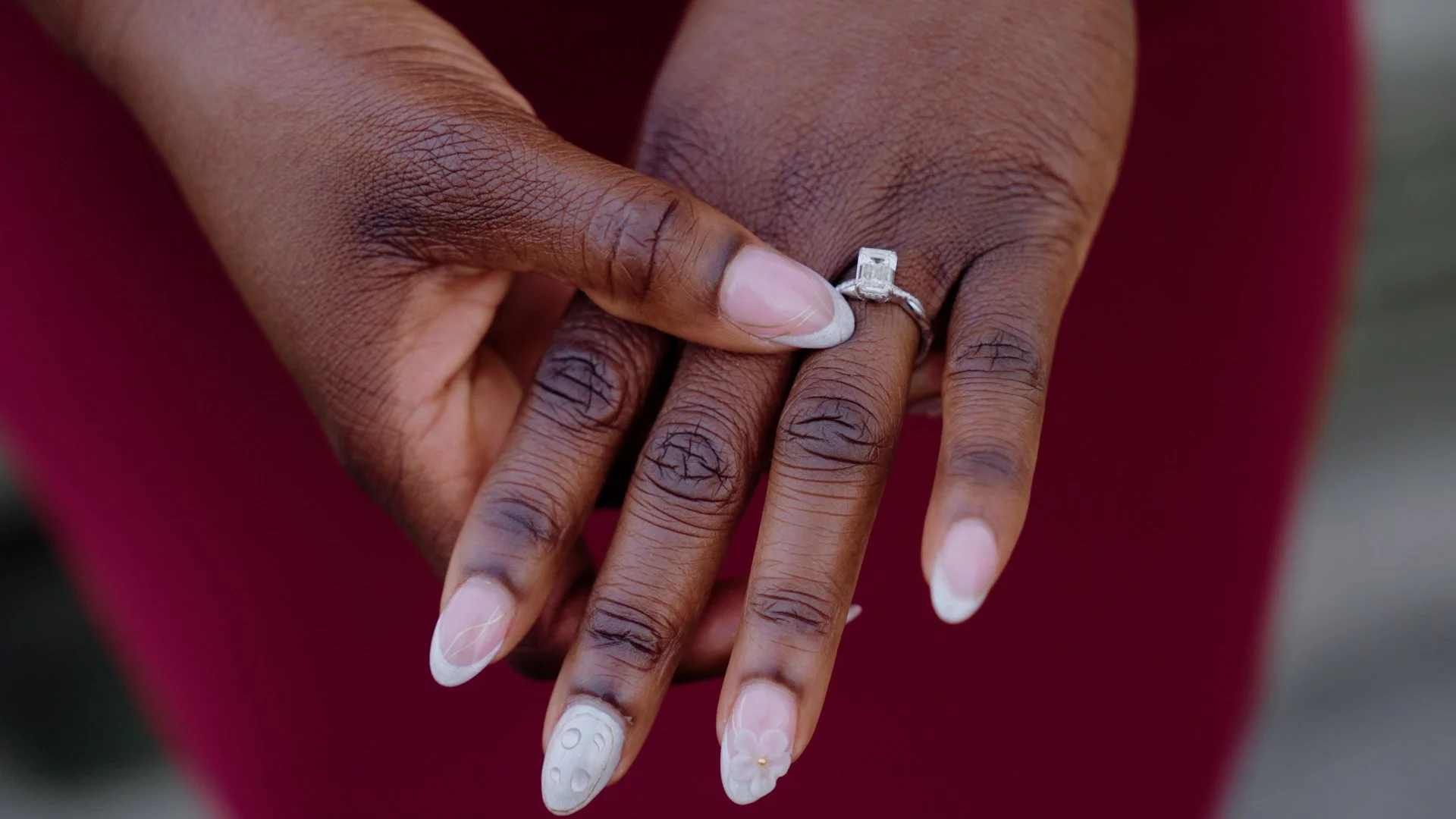 Close-up of Moyo's hands holding each other, one hand wearing a diamond engagement ring.