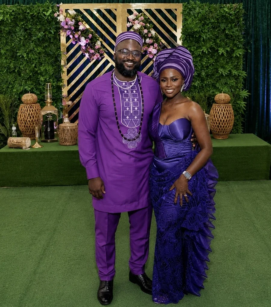 Liam and Moyo, dressed in traditional African attire, smile and pose together at a decorated event.