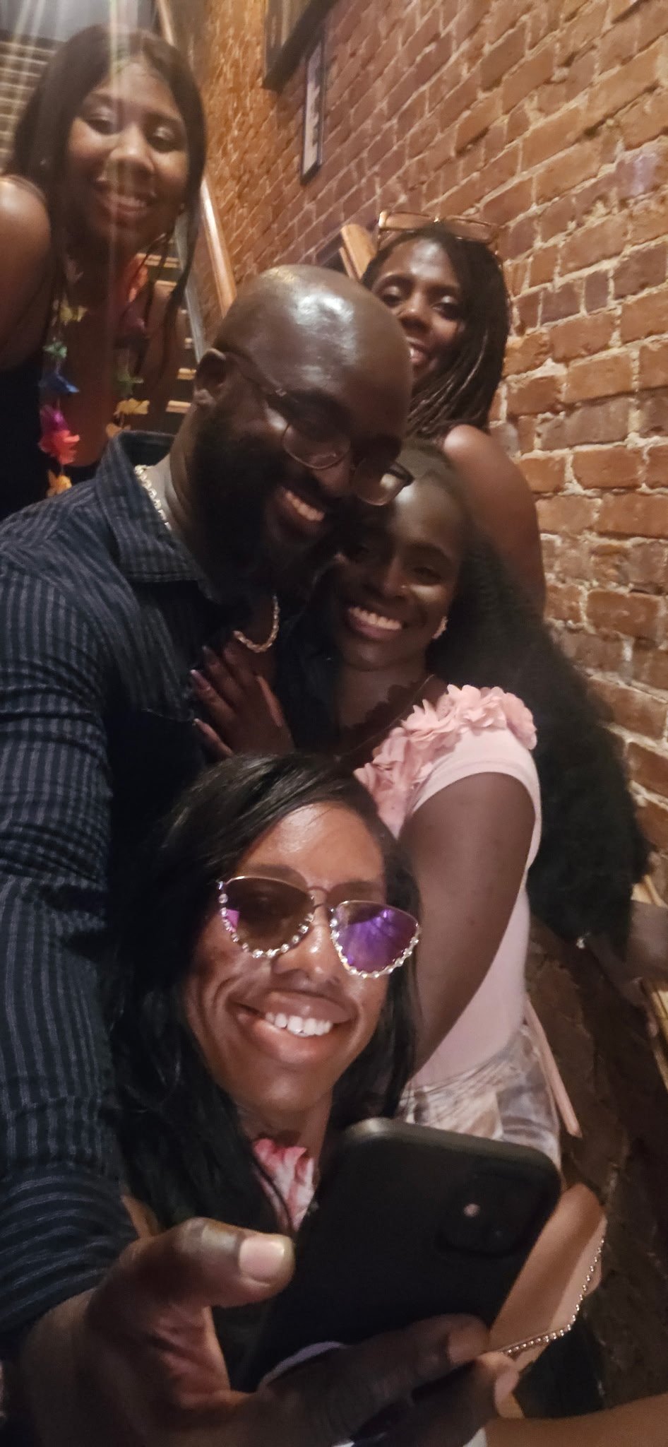 Moyo and Liam with friends taking a selfie together in front of a brick wall, smiling and having fun.