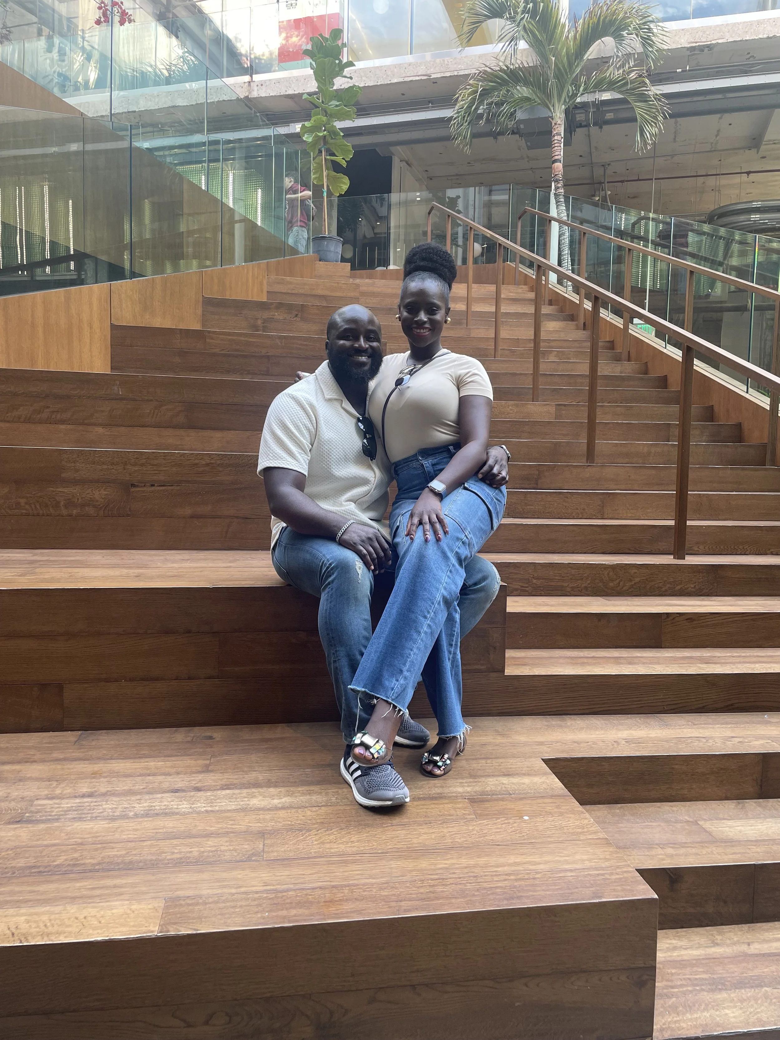 Liam and Moyo are sitting on wooden stairs indoors, smiling for the camera.